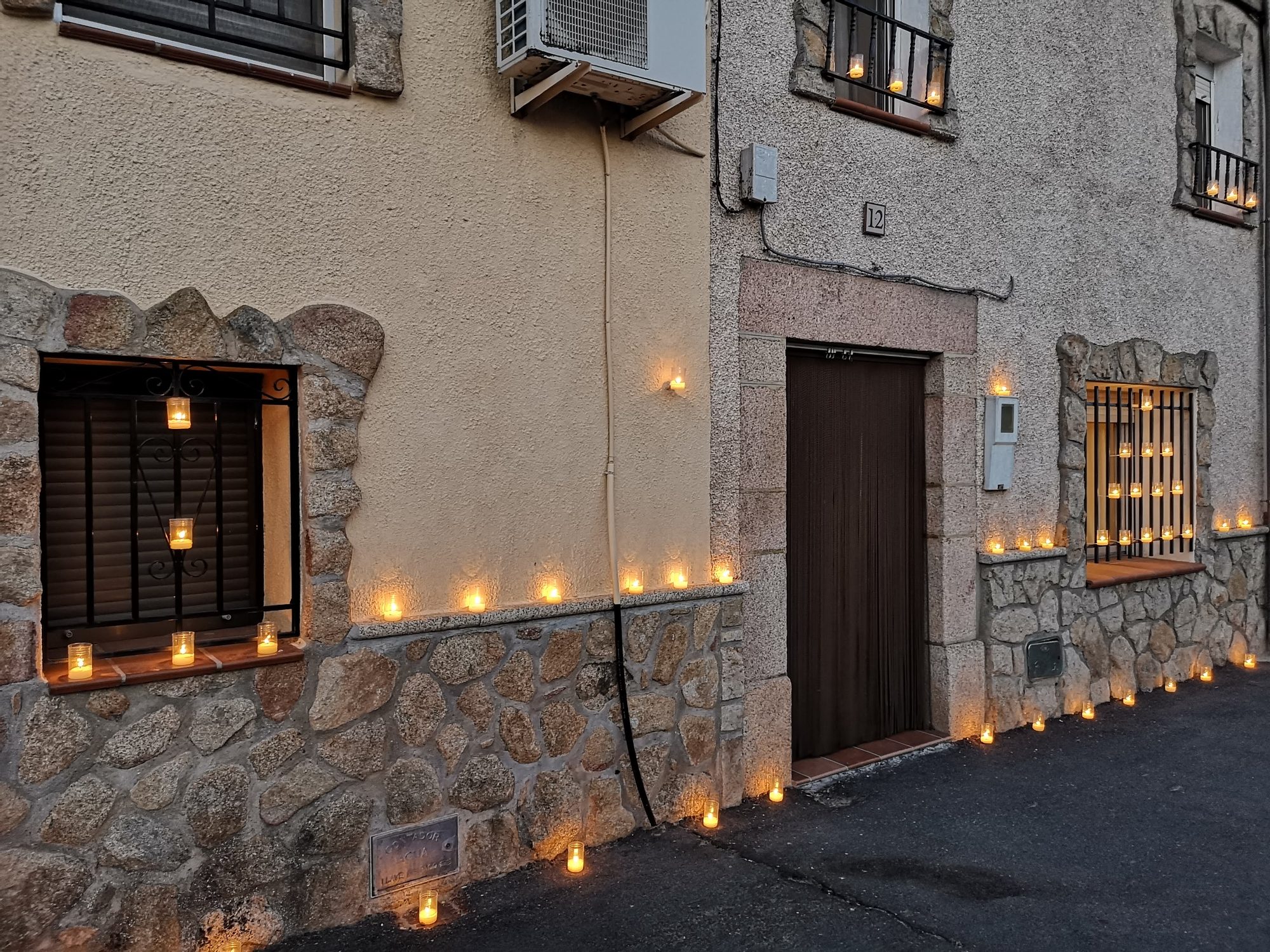 Fachada tradicional de piedra iluminada con decenas de velas en ventanas y suelo.