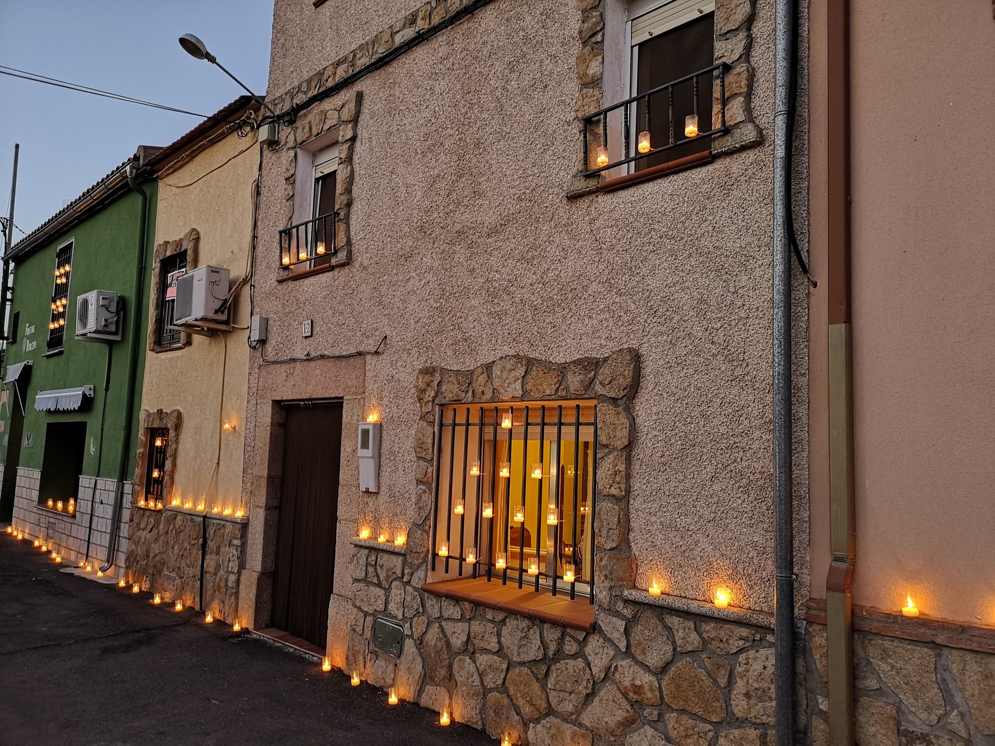 Fachadas de casas de pueblo decoradas con cientos de velas encendidas al anochecer.