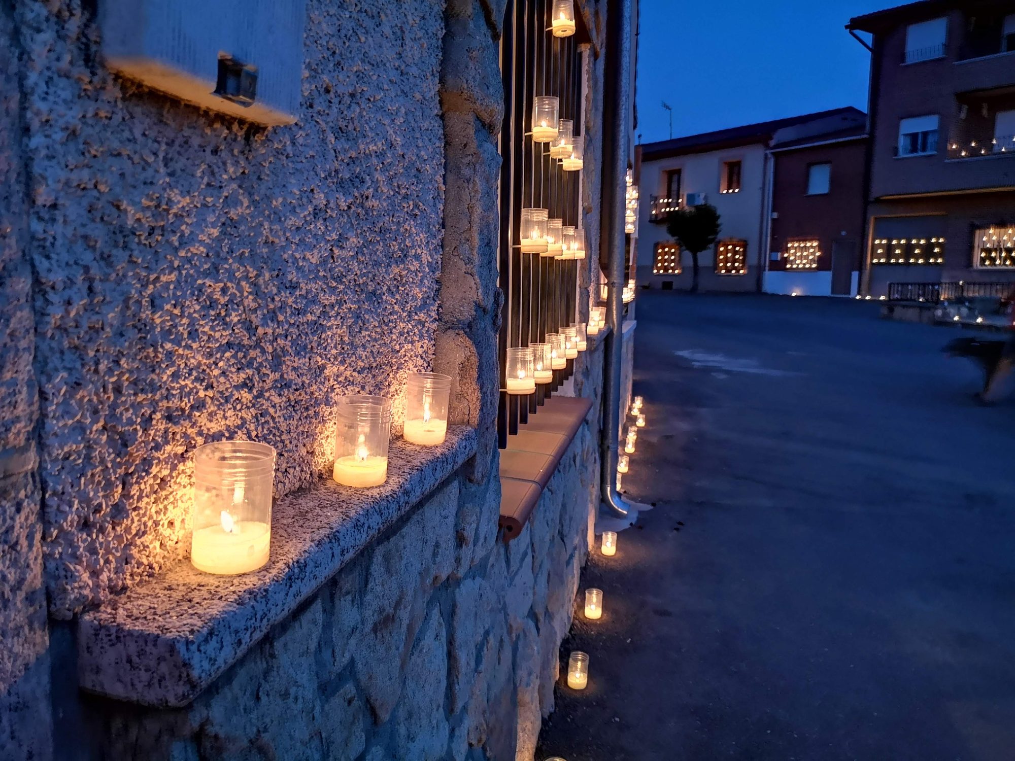 Velas encendidas en tarros de cristal decorando la fachada de una casa al anochecer.