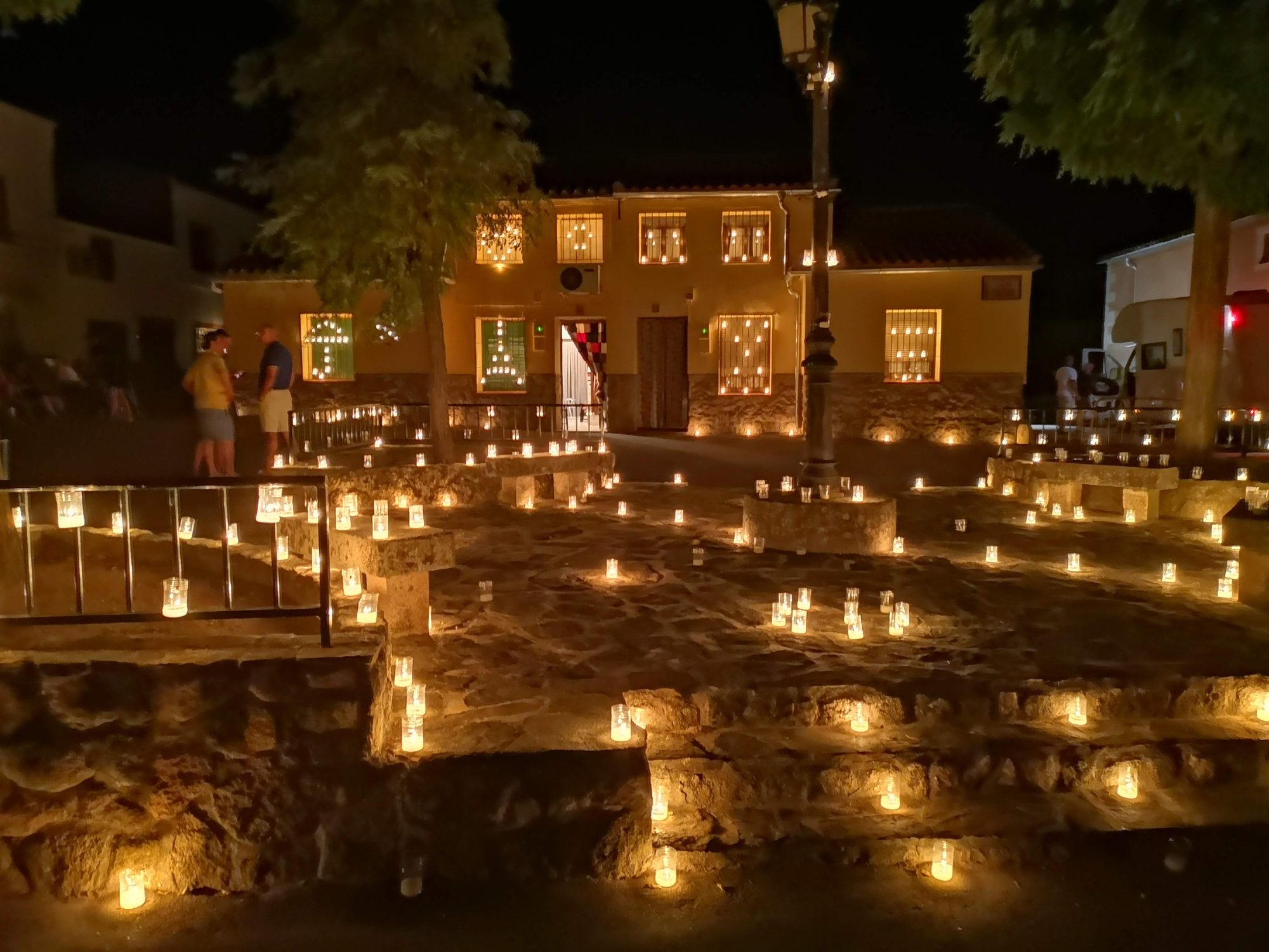 Plaza empedrada iluminada por cientos de velas nocturnas frente a un edificio tradicional.