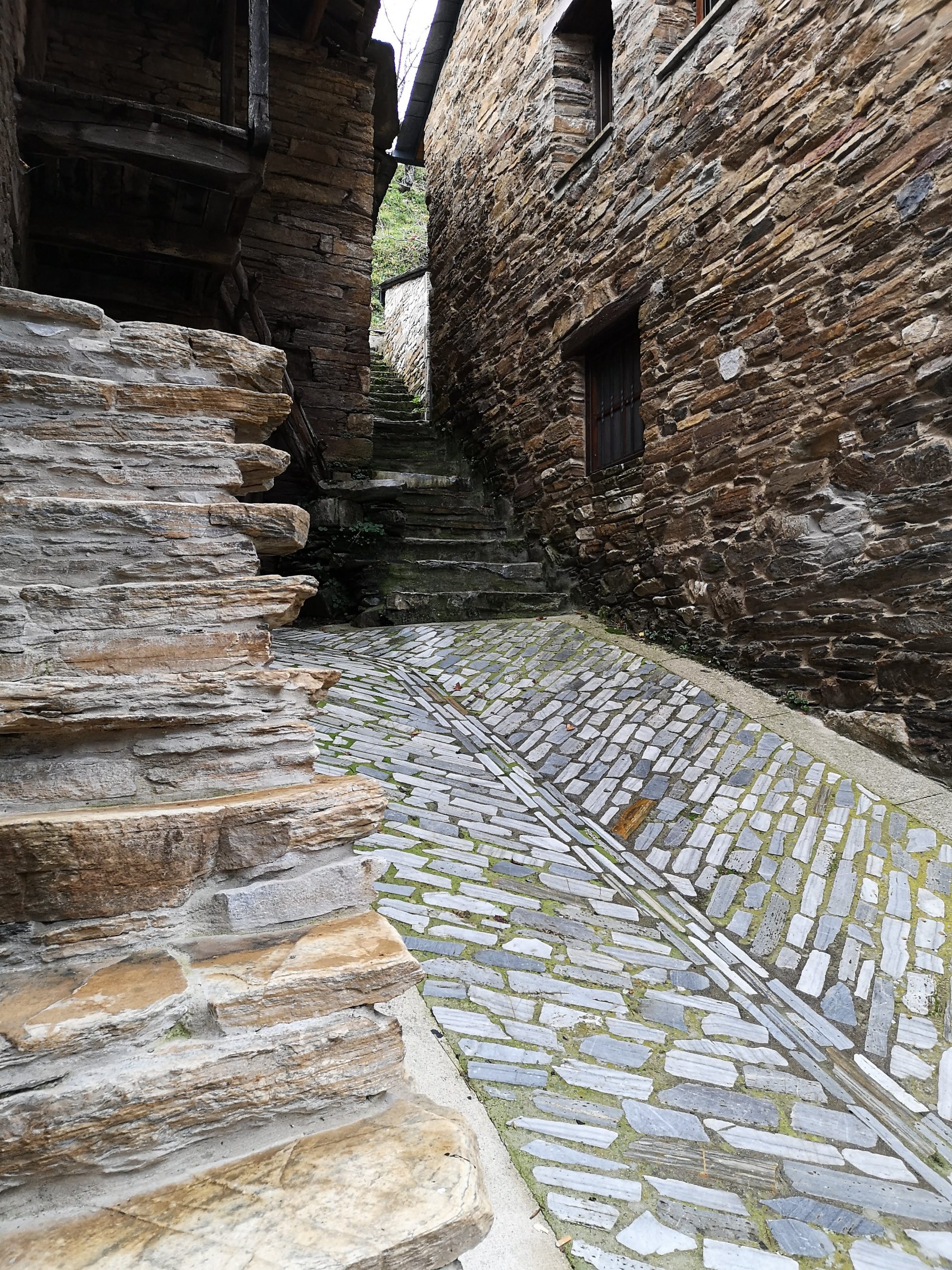 Calle empedrada con escaleras entre casas tradicionales de piedra y pizarra.