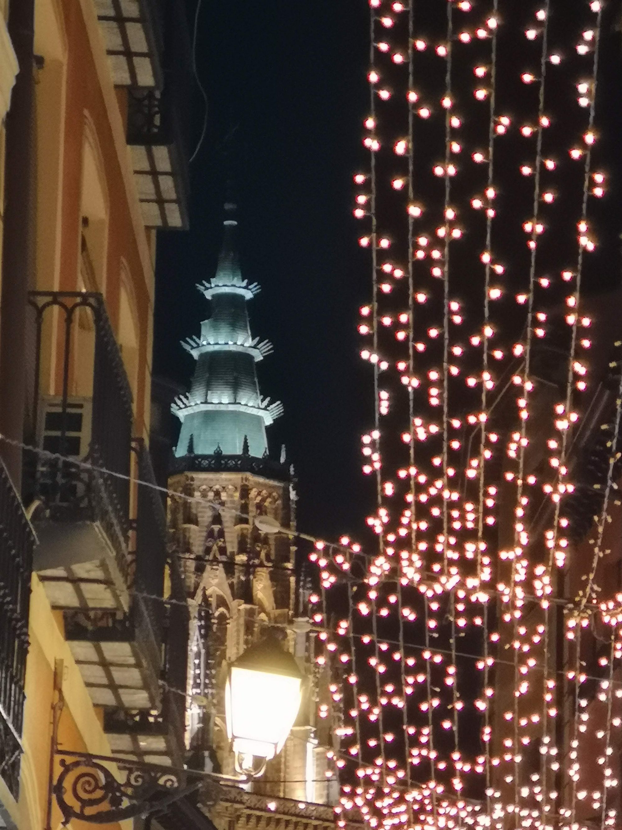 Torre de la Catedral de Toledo iluminada de noche entre calles con luces navideñas.