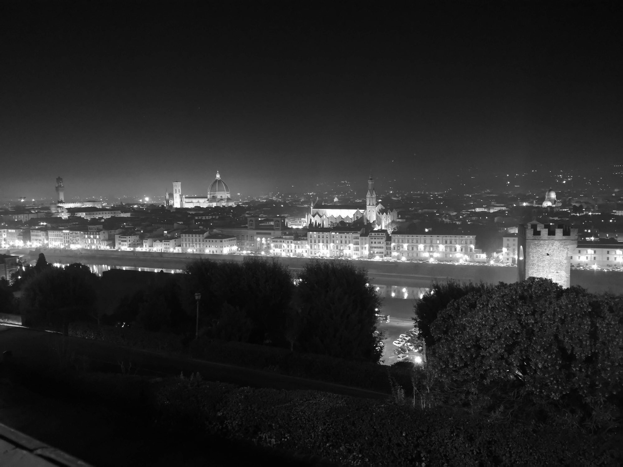 Vista nocturna en blanco y negro de Florencia con la catedral iluminada al fondo.