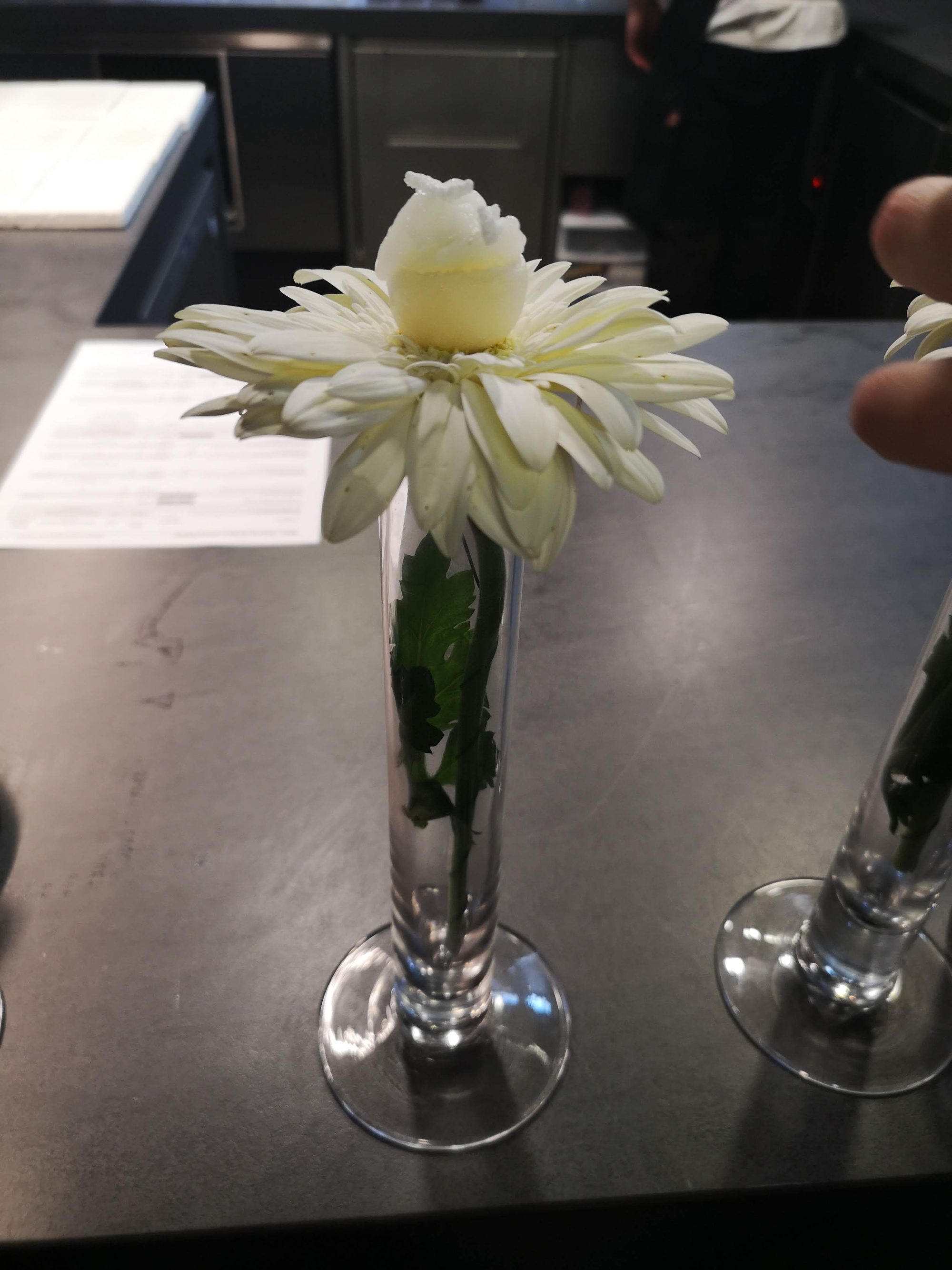 Flor blanca en probeta de cristal con bocado gastronómico en el centro.