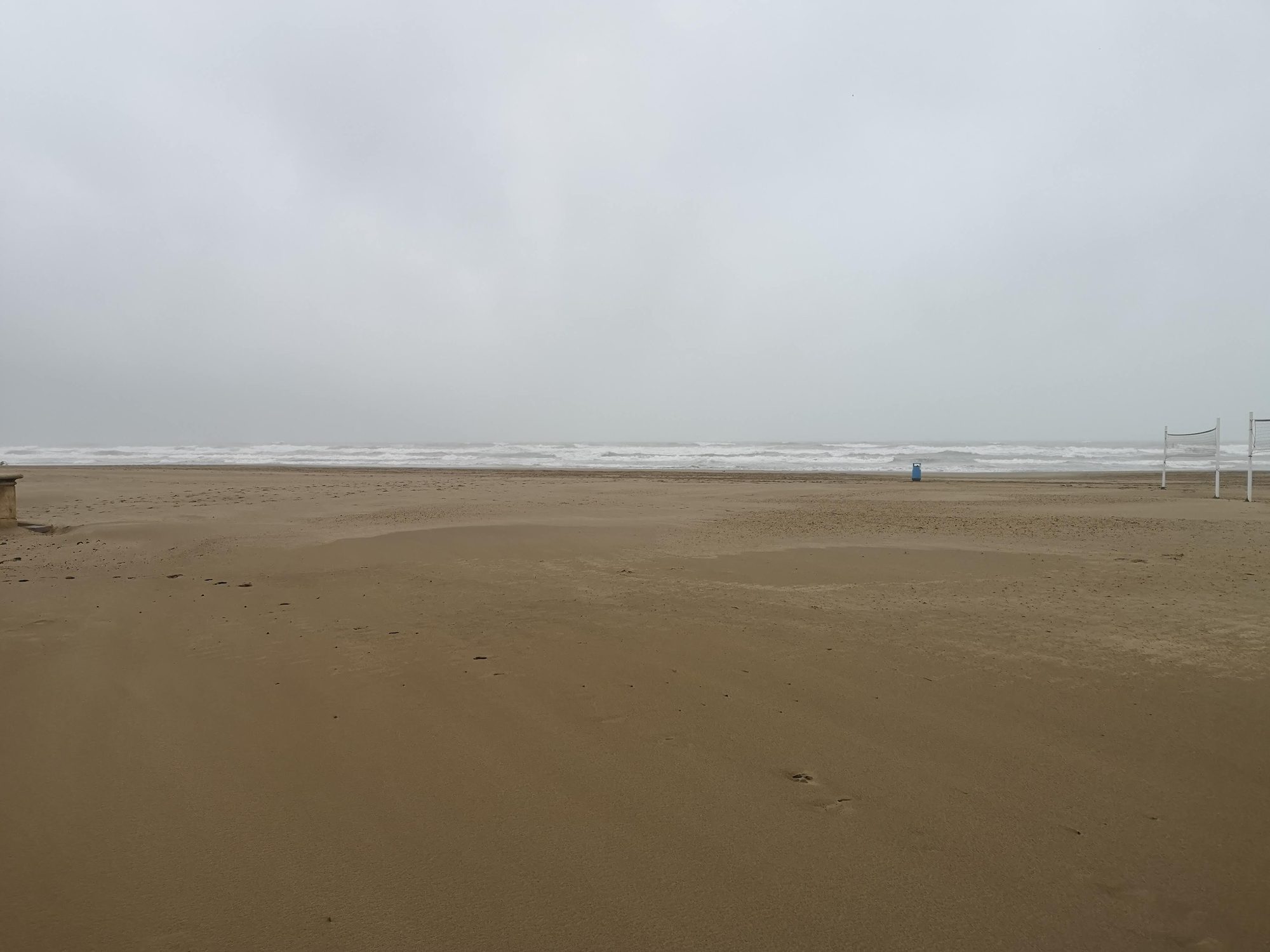 Playa de arena desierta y mar embravecido bajo un cielo completamente nublado y gris.