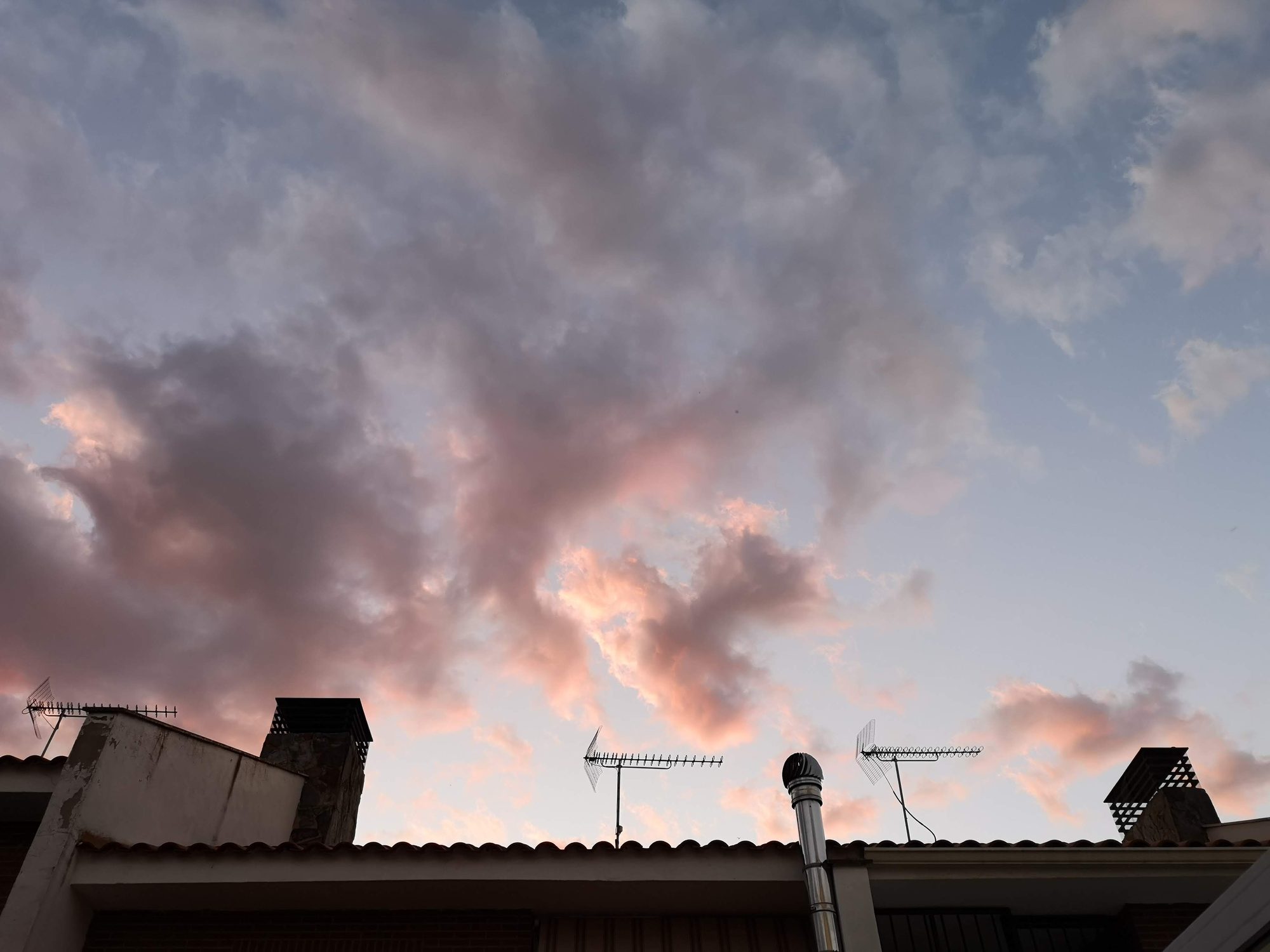 Nubes teñidas de rosa al atardecer sobre los tejados y antenas de Bargas.