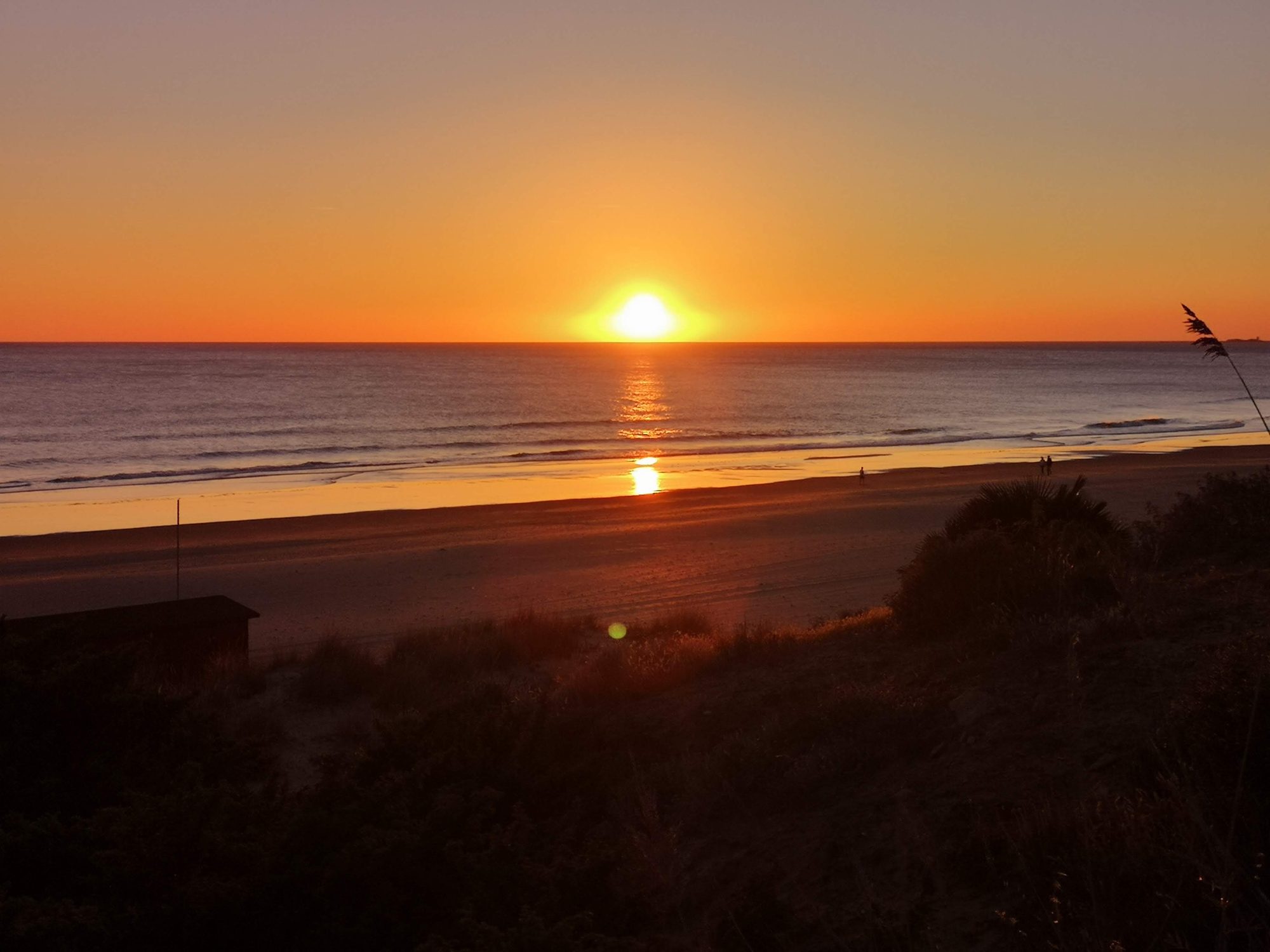 Puesta de sol dorada sobre el mar y la amplia orilla de la playa.