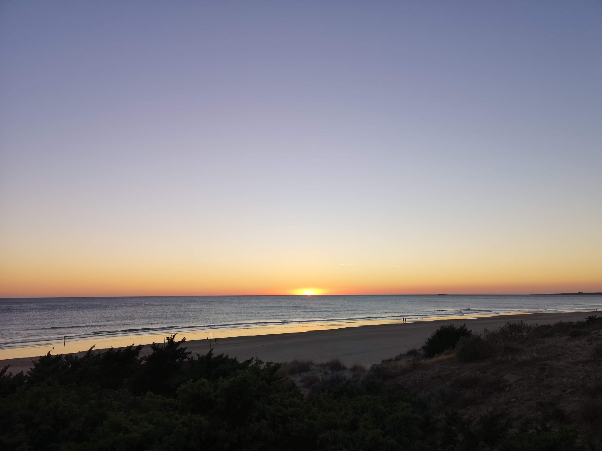 Atardecer dorado sobre la amplia playa y el mar bajo un cielo despejado.