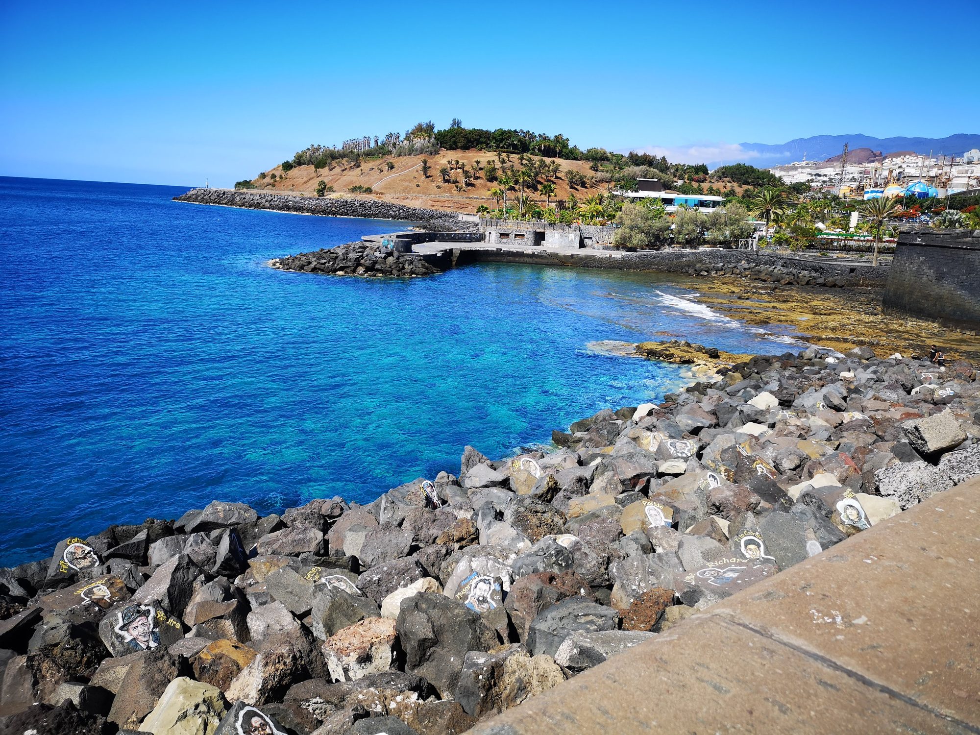 Rocas con retratos pintados frente a aguas turquesas en la costa de Tenerife.
