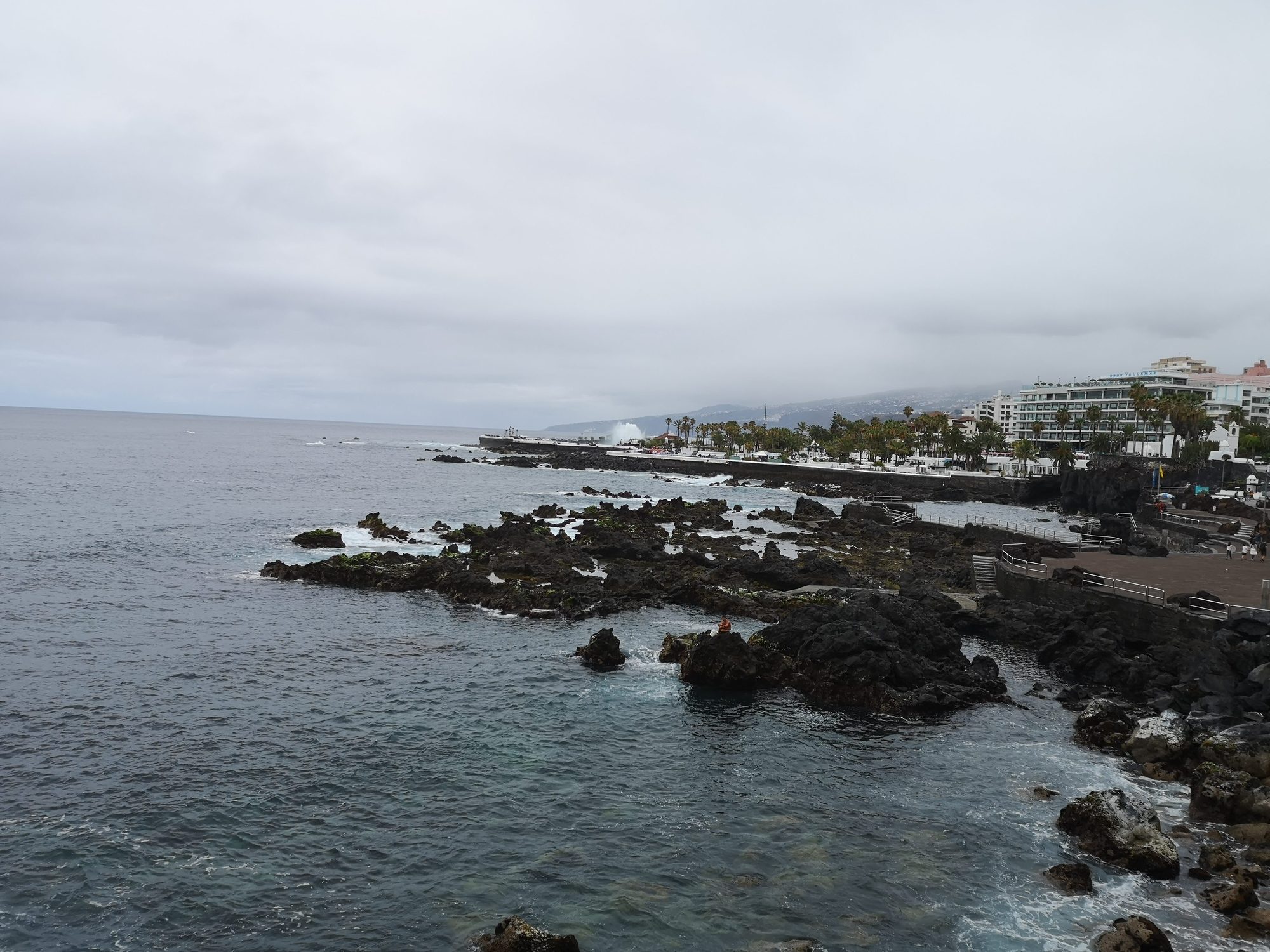 Costa de rocas volcánicas negras frente al mar y paseo marítimo con edificios.