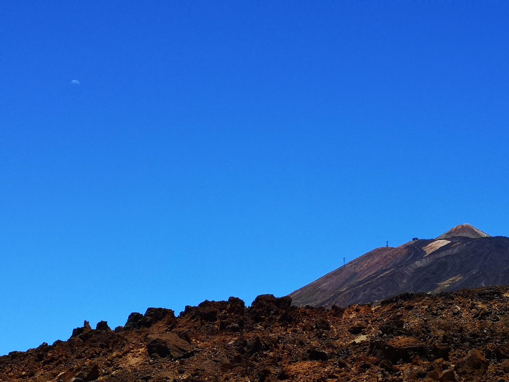 Paisaje volcánico del Teide bajo un cielo azul intenso con la luna visible.