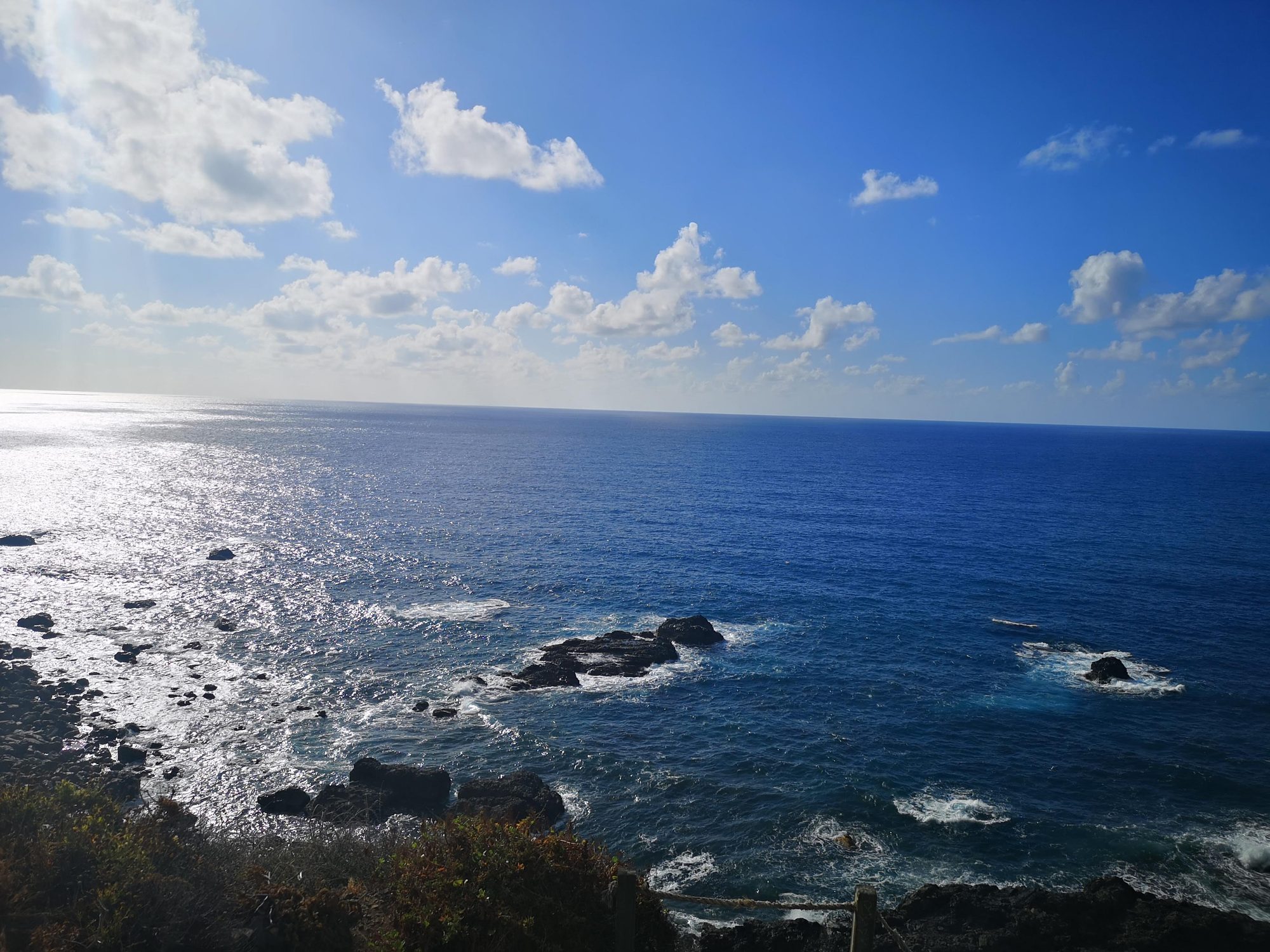 Océano Atlántico y costa rocosa con reflejos de sol bajo un cielo con nubes.