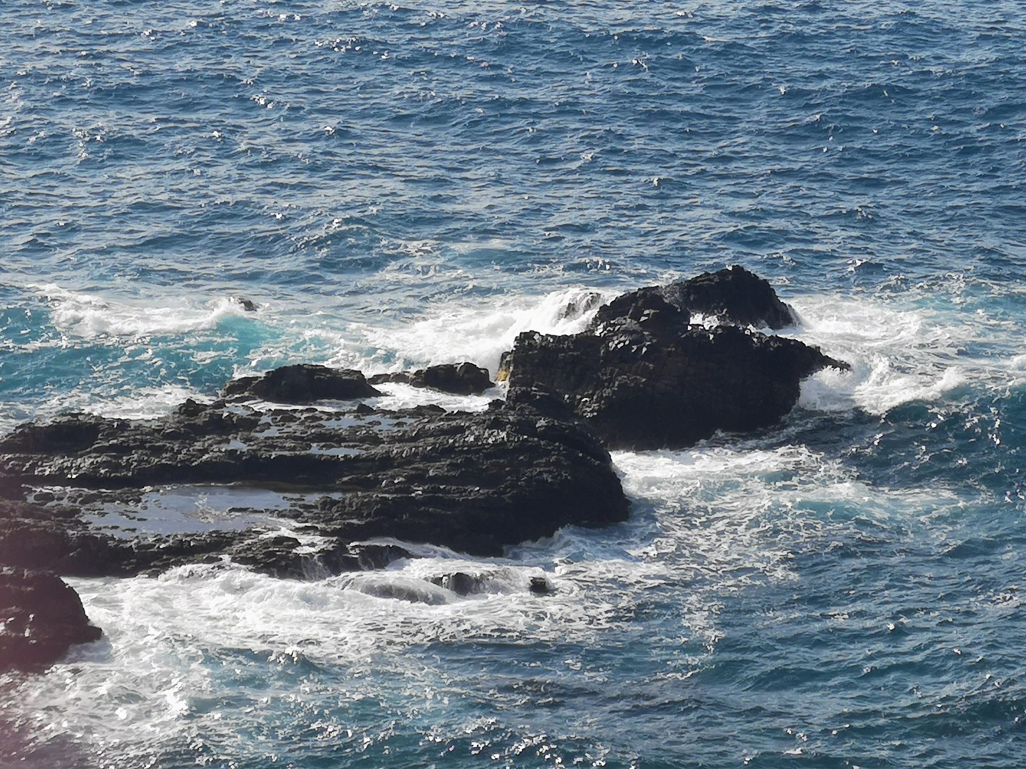 Olas del mar rompiendo con fuerza contra formaciones de roca volcánica oscura.