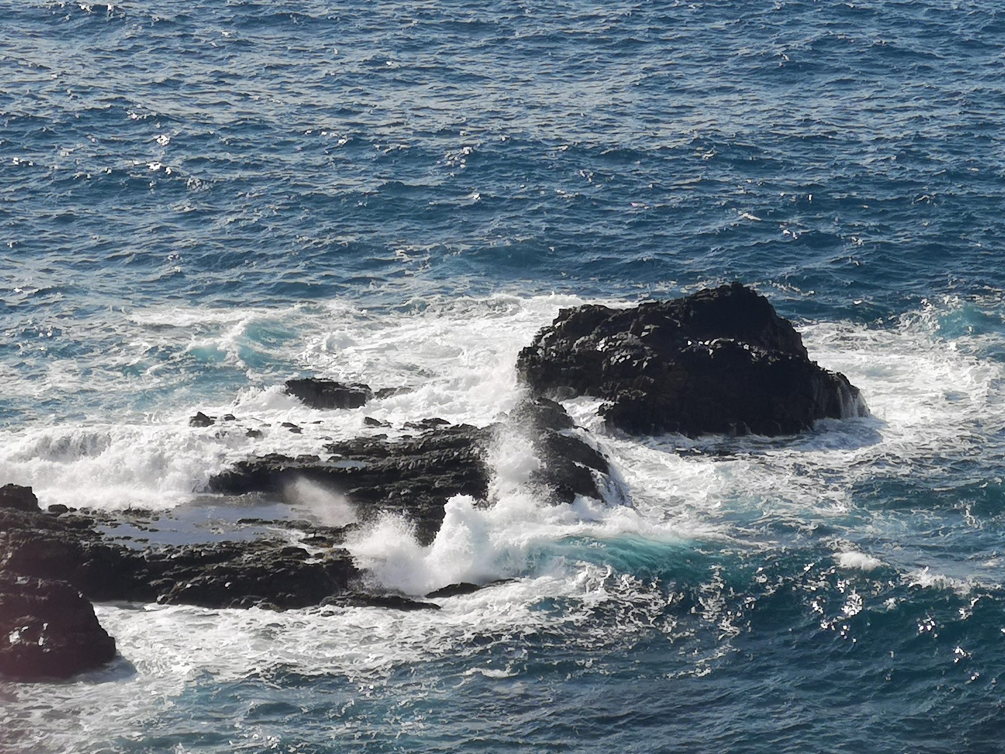 Olas del océano rompiendo con fuerza contra oscuras rocas volcánicas en la costa marina.