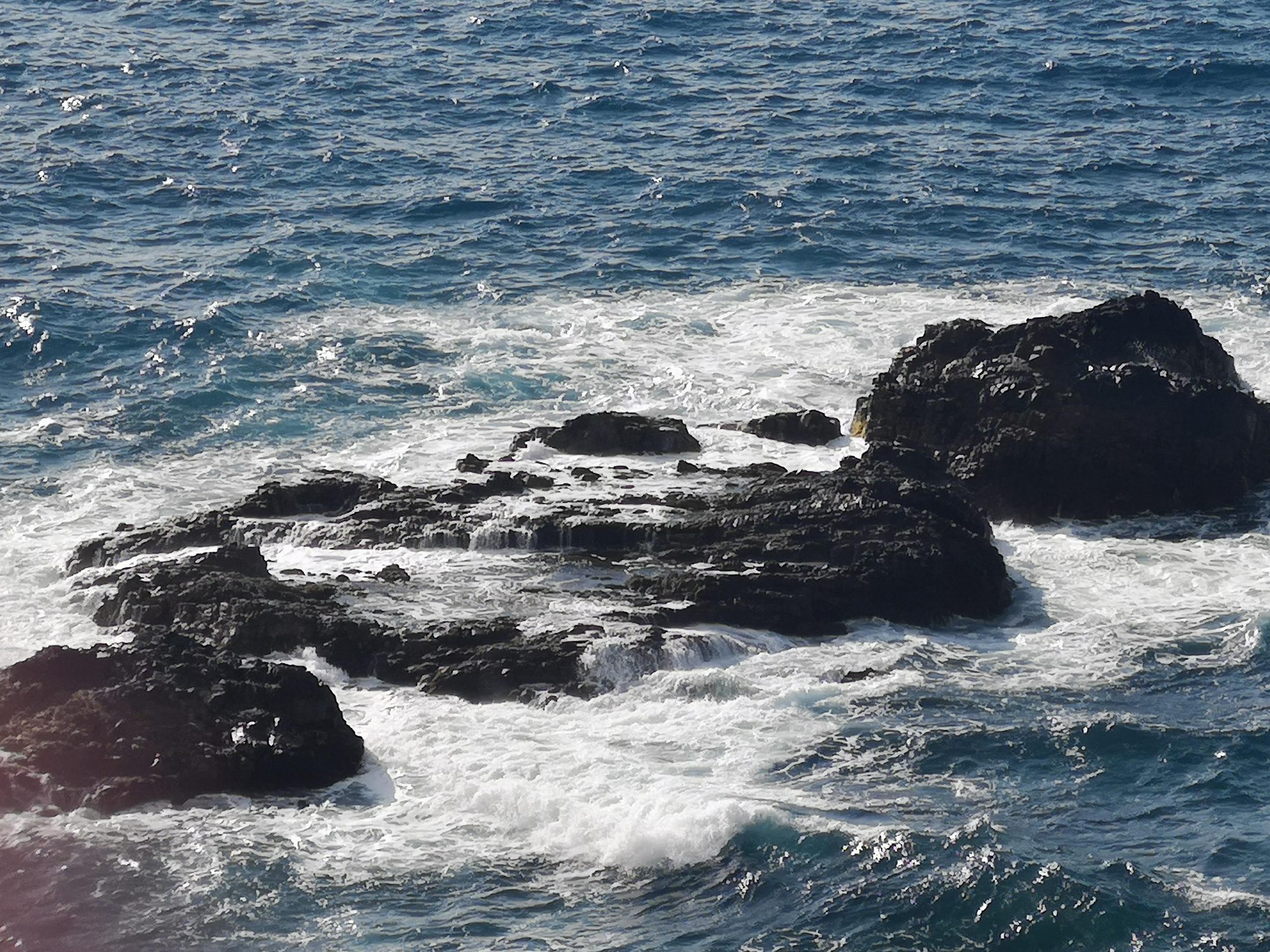 Olas del mar Atlántico rompiendo con fuerza contra rocas volcánicas oscuras.