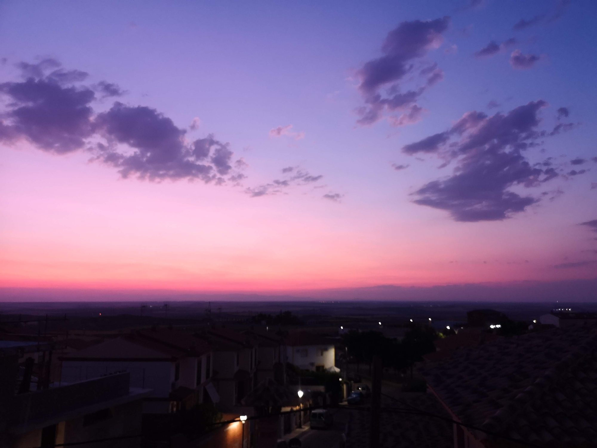 Atardecer con cielo en tonos violetas y rosas sobre los tejados de un pueblo.