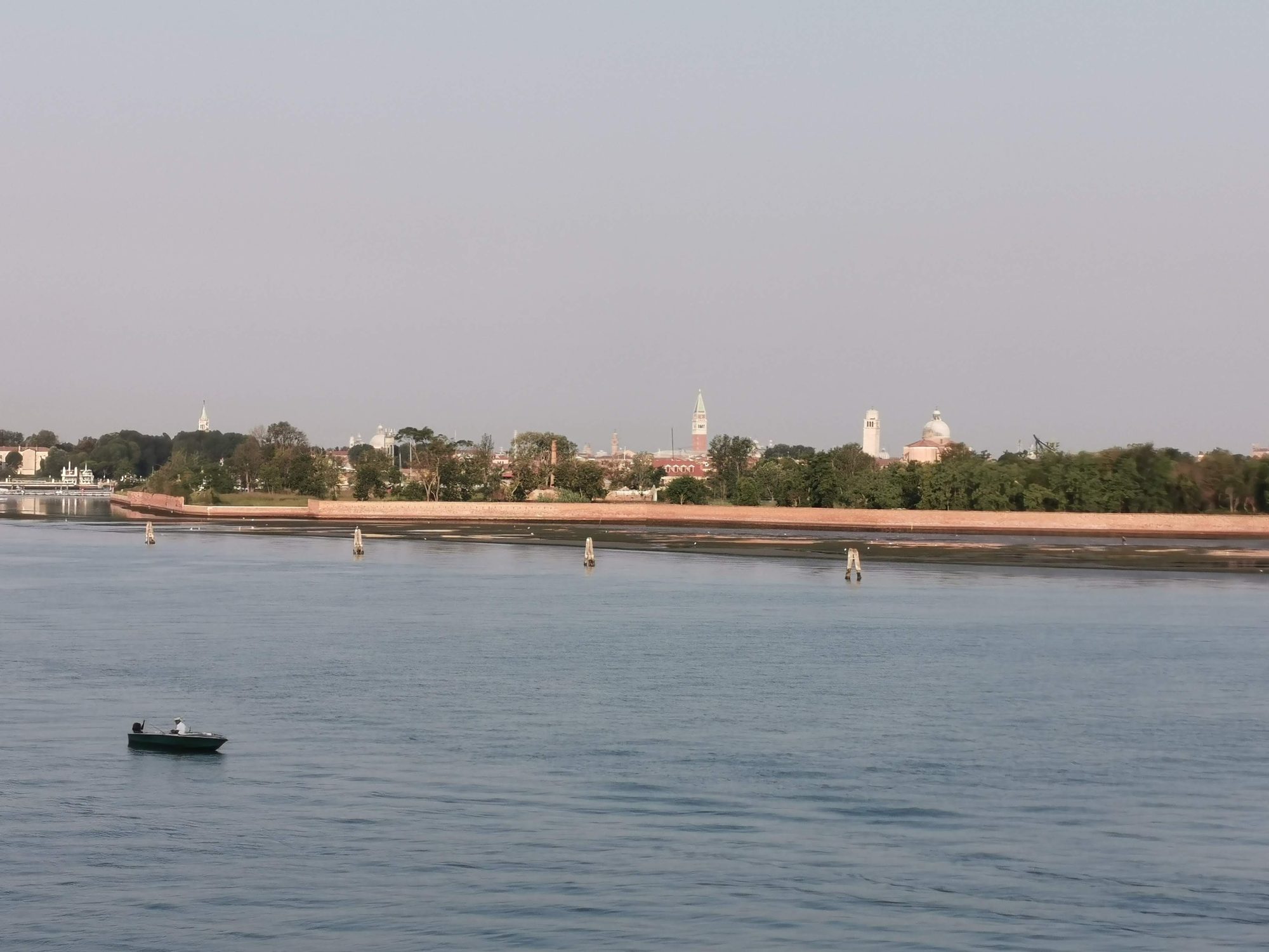 Vista panorámica de la laguna de Venecia con una pequeña barca y campanarios lejanos.