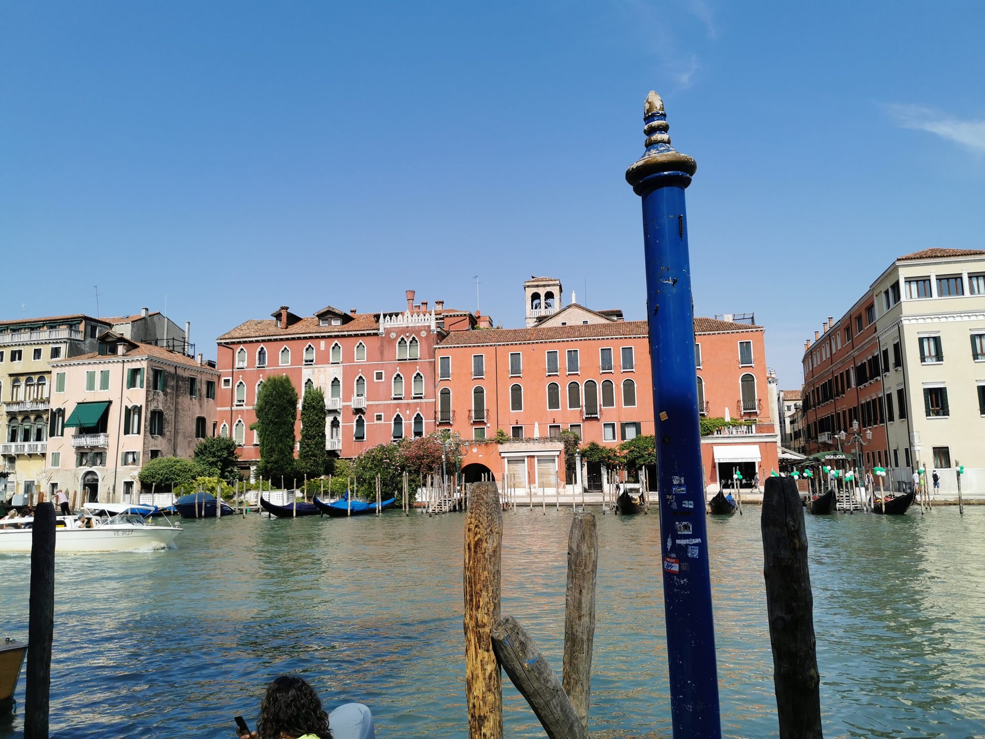 Canal de Venecia con edificios históricos color terracota, góndolas amarradas y poste azul.