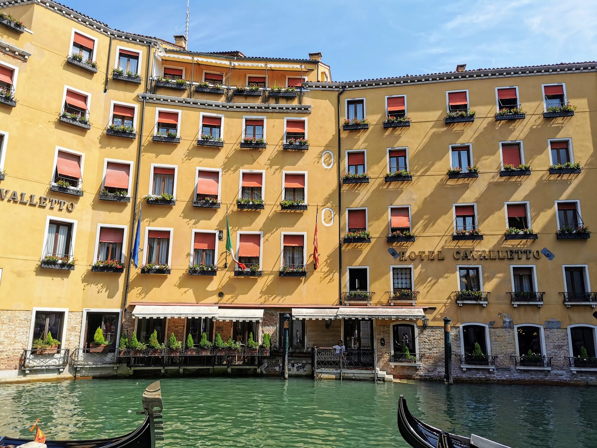 Fachada amarilla del Hotel Cavalletto frente a un canal de Venecia con góndolas.
