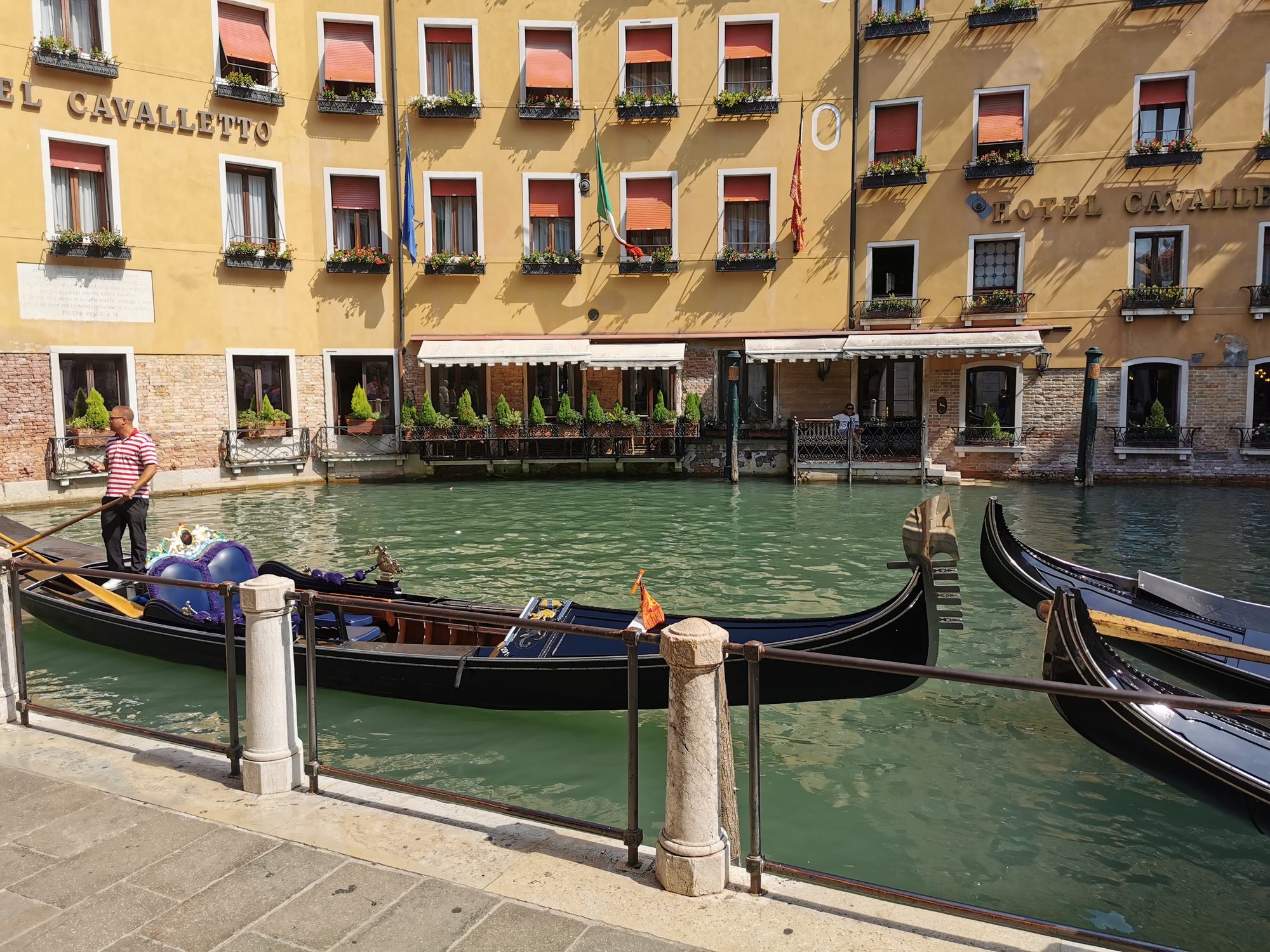 Góndolas amarradas en un canal de Venecia frente a un edificio histórico amarillo.