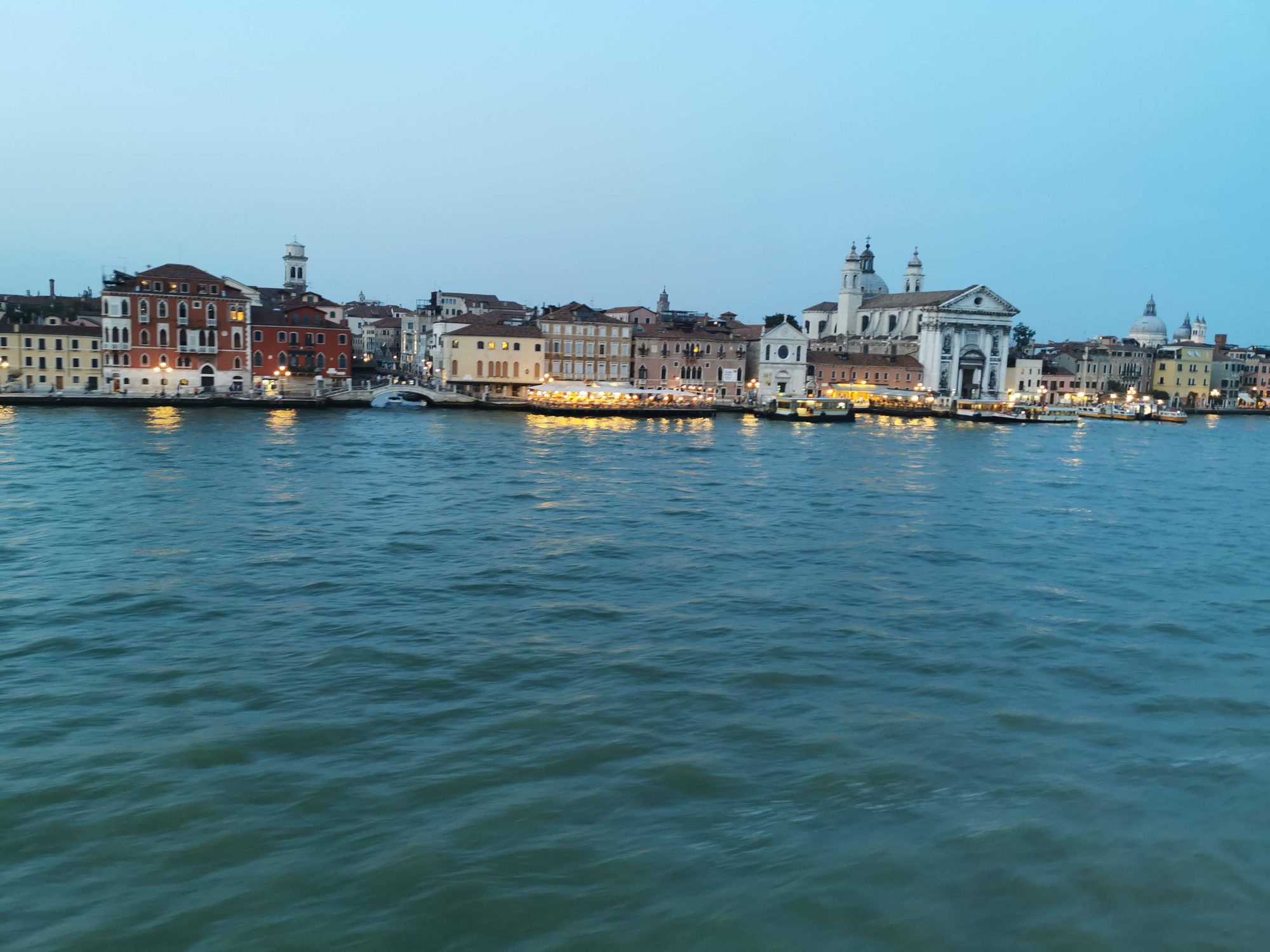 Vista panorámica de edificios históricos e iglesias iluminadas frente al canal en Venecia.