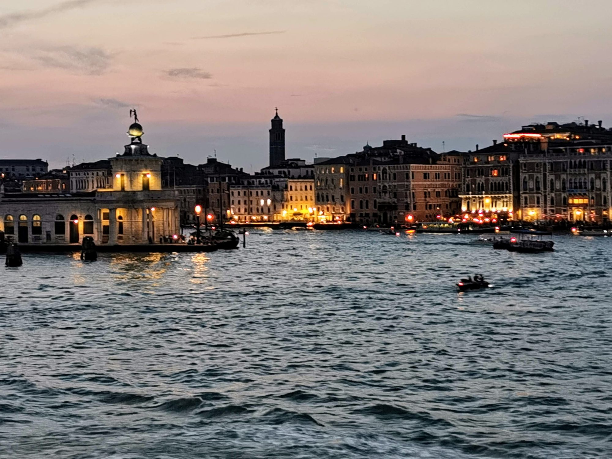 Punta della Dogana y edificios iluminados al atardecer en las aguas de Venecia.