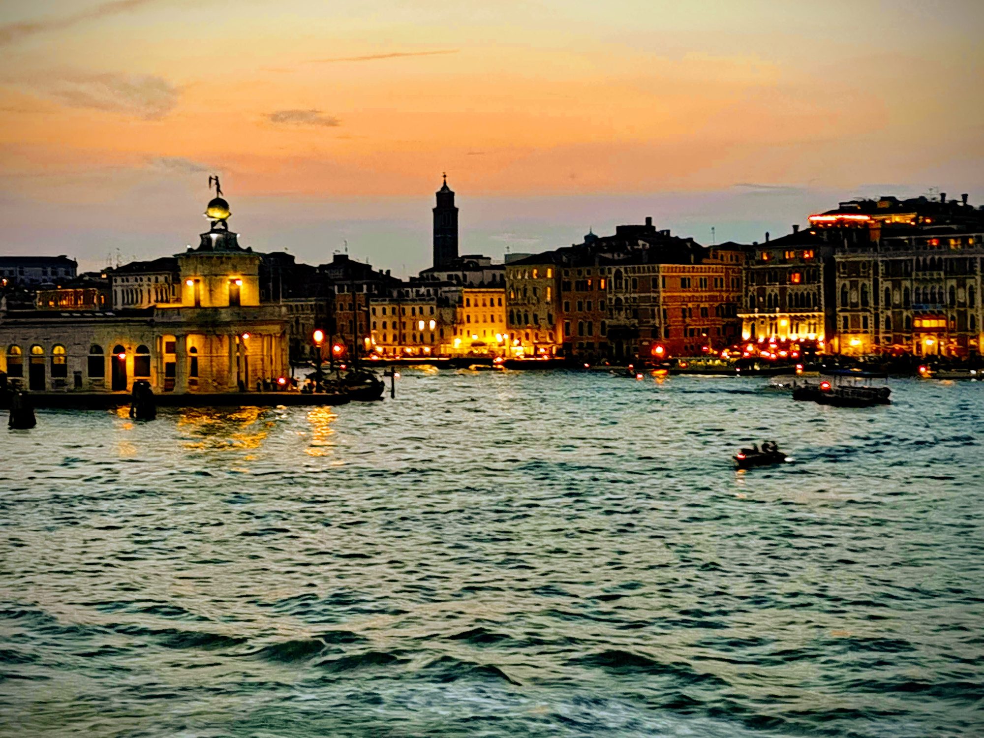 Atardecer sobre el canal en Venecia con la Punta della Dogana iluminada y edificios históricos.