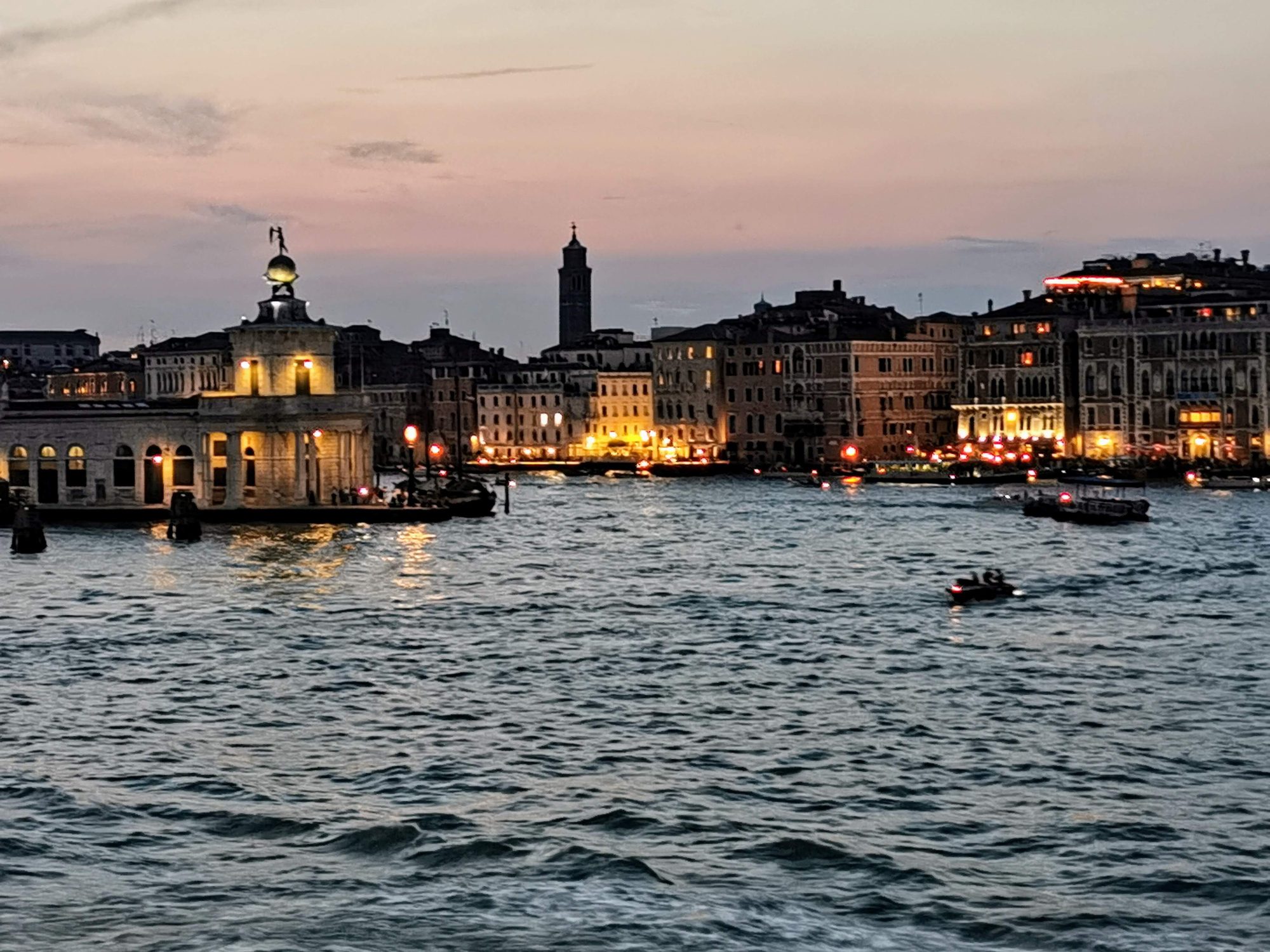 Punta della Dogana y edificios iluminados frente a la laguna de Venecia al anochecer.