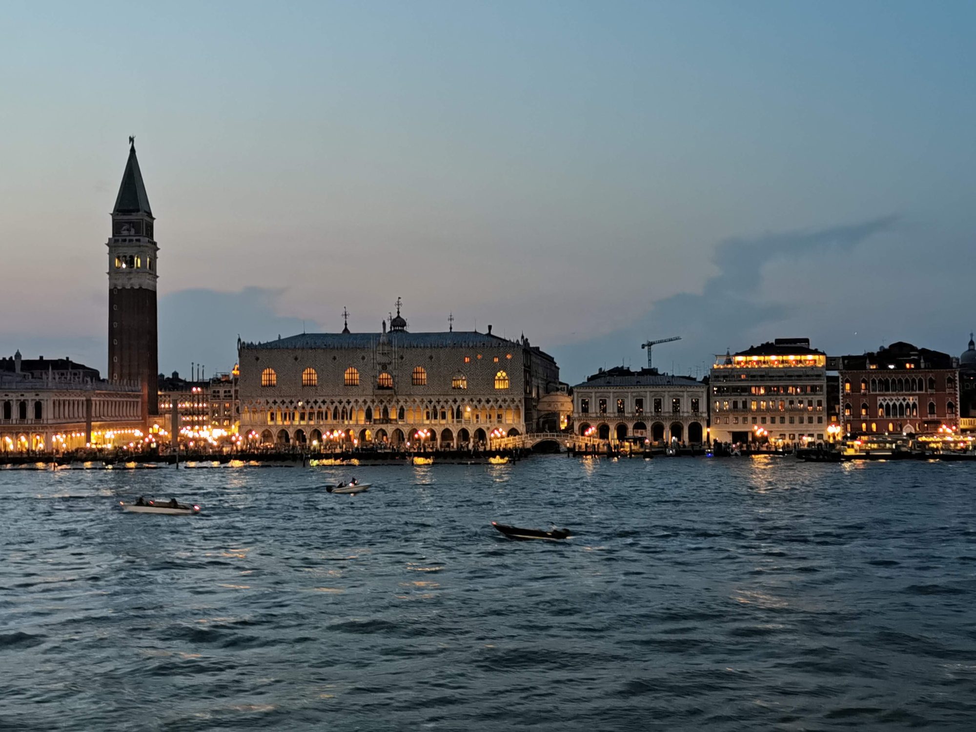 Plaza de San Marcos y Palacio Ducal iluminados al anochecer desde el agua en Venecia.