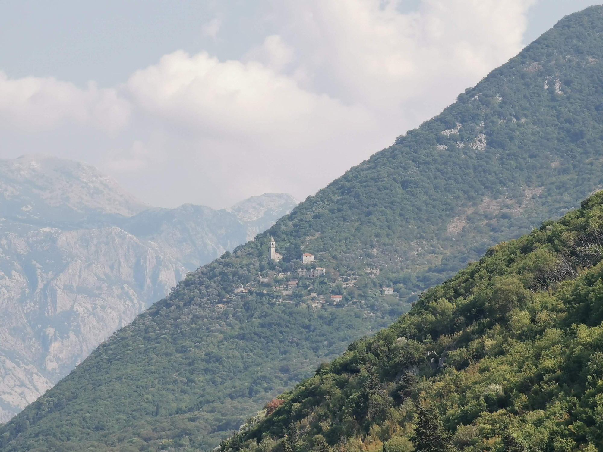 Campanario y casas tradicionales en una ladera verde rodeada de imponentes montanas