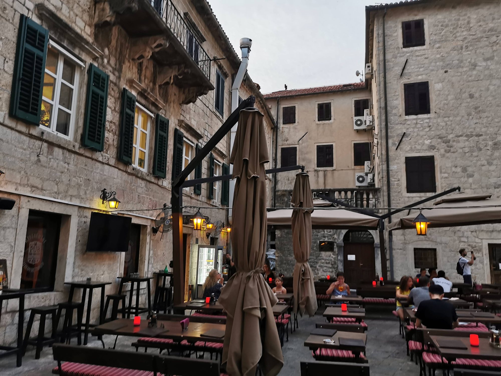 Terraza de restaurante con mesas de madera entre edificios históricos de piedra en Kotor.