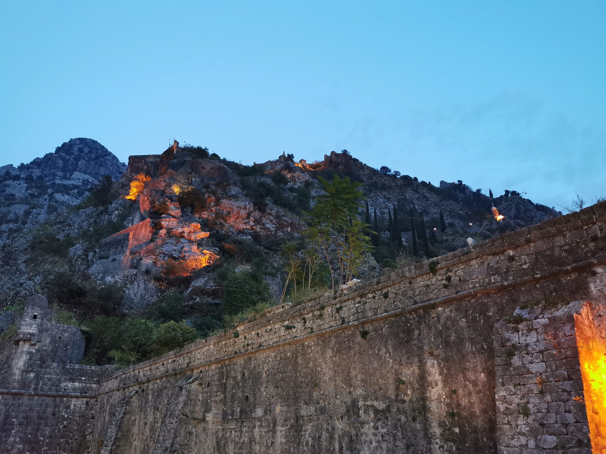 Murallas históricas iluminadas en la ladera de la montaña en Kotor al anochecer.