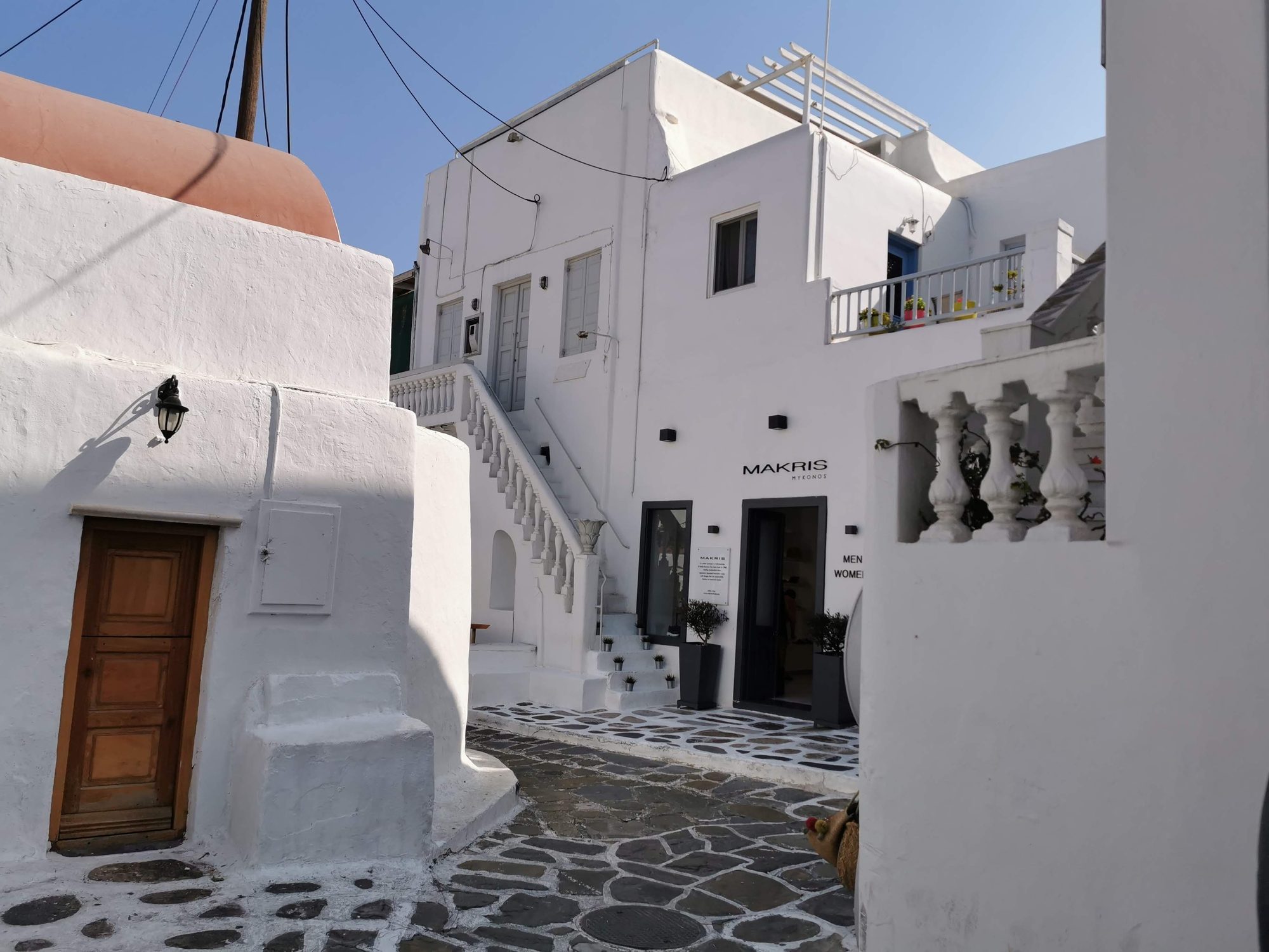 Calle empedrada con casas blancas tradicionales de arquitectura cicládica bajo el sol en Miconos.