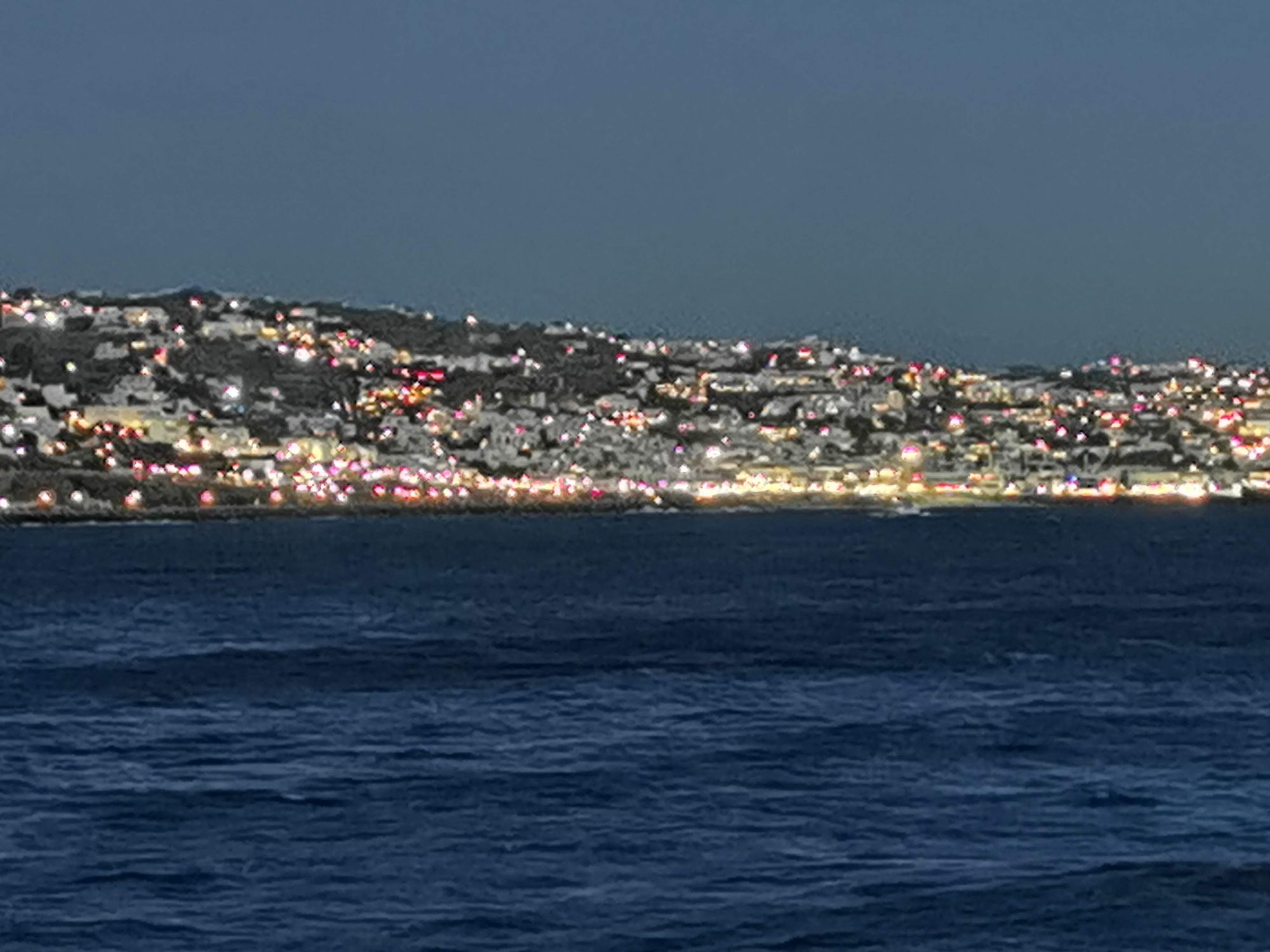 Luces nocturnas de la costa y casas iluminadas frente al mar azul oscuro.