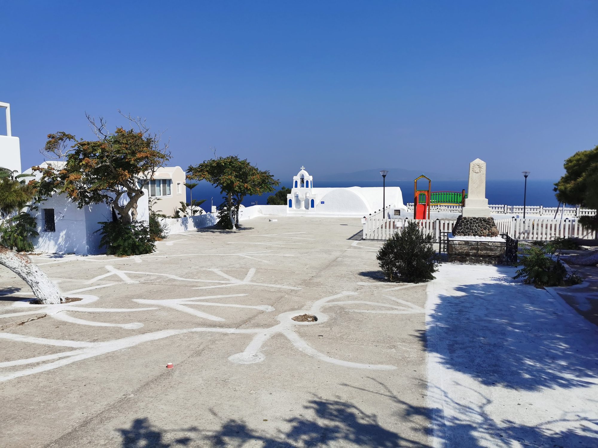 Plaza blanca tradicional con pequeña iglesia y vistas al mar Egeo en Oia.