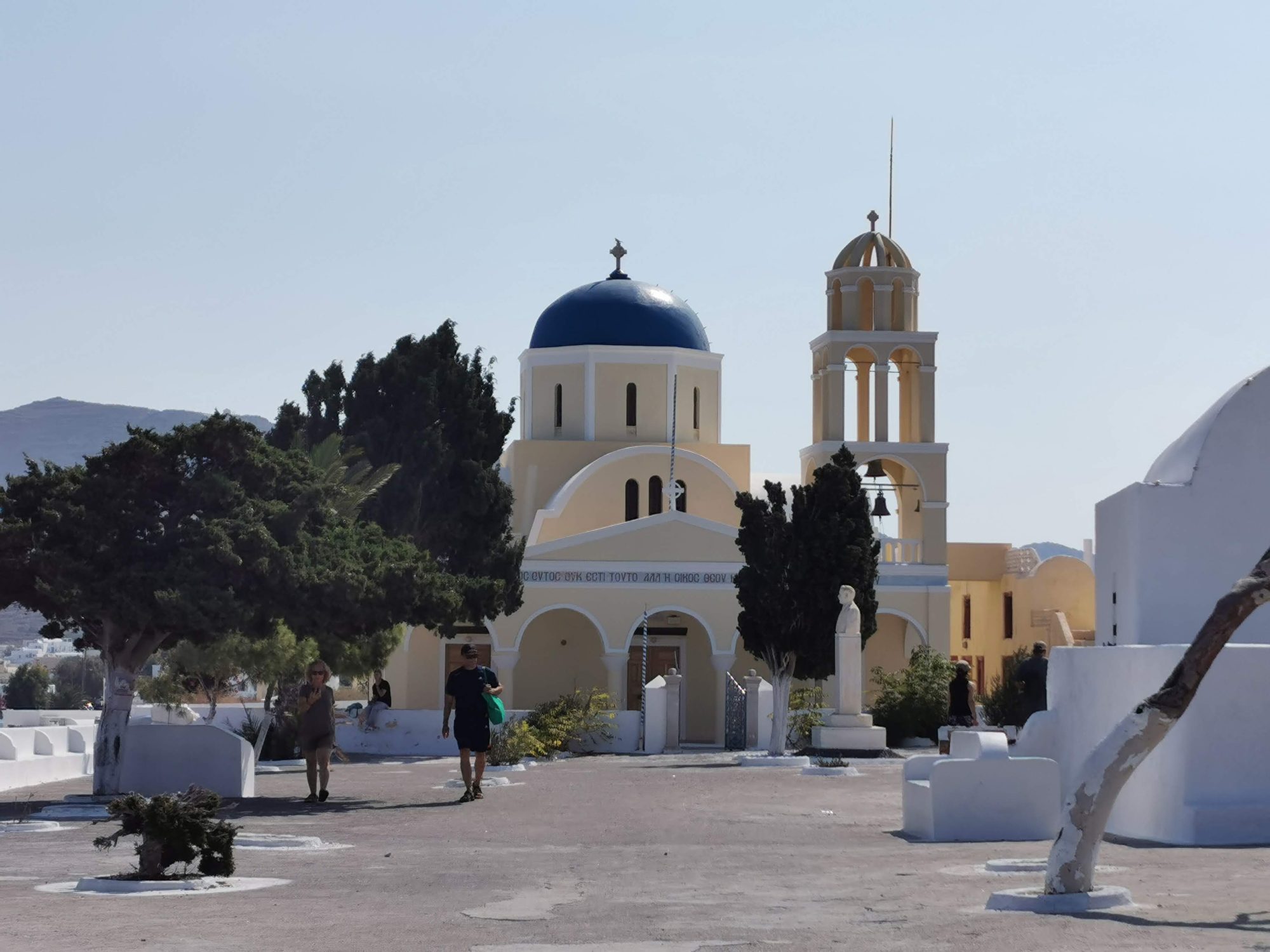 Iglesia ortodoxa con cúpula azul y campanario en la plaza de Oia.