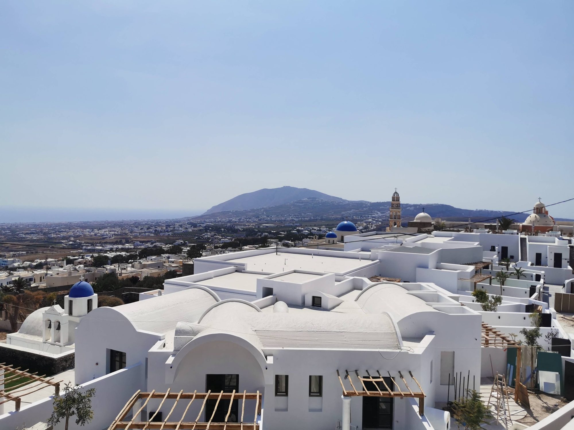 Casas blancas tradicionales con cúpulas azules y colinas al fondo en Santorini, Grecia.
