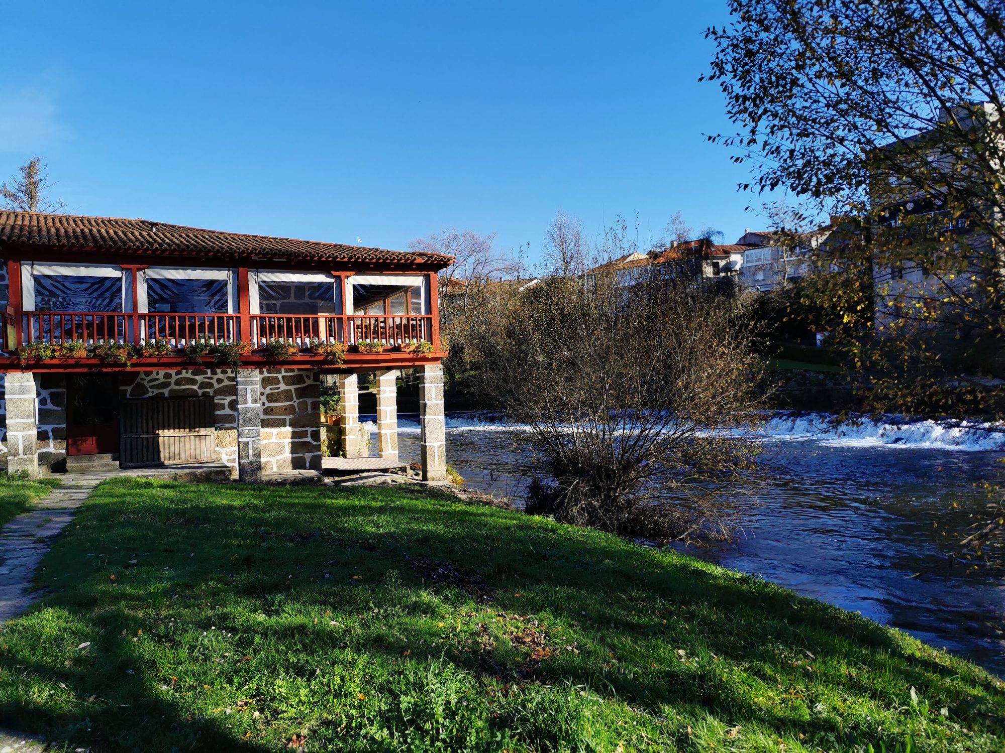 Casa tradicional de piedra junto al río Arnoia con césped y cielo despejado.