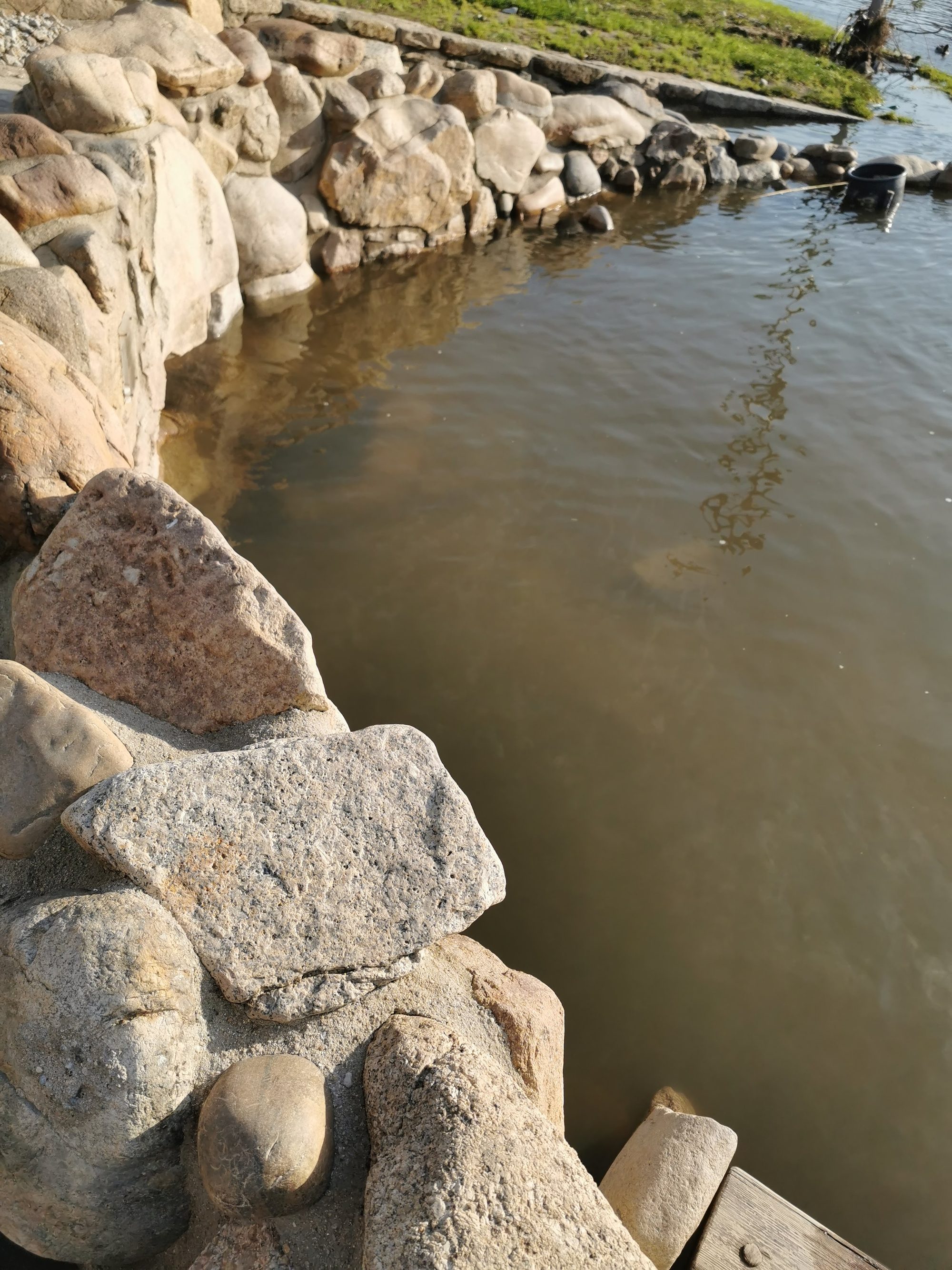 Muro de piedras naturales al borde de un estanque de agua tranquila y calmada.