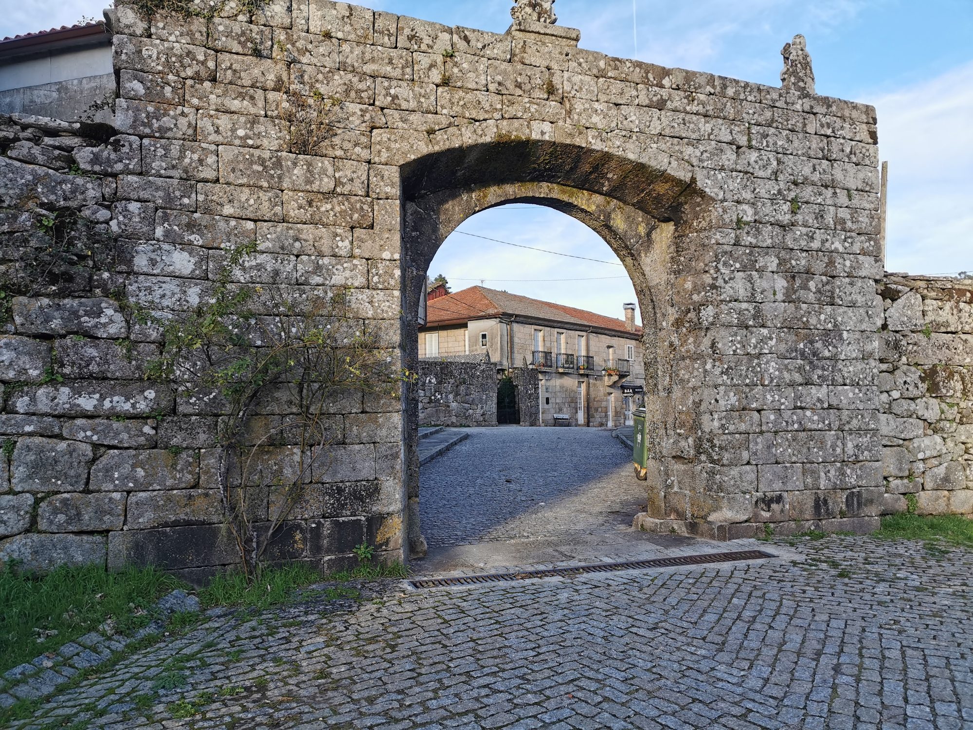 Arco de piedra antiguo con vista a una calle empedrada y casas tradicionales.