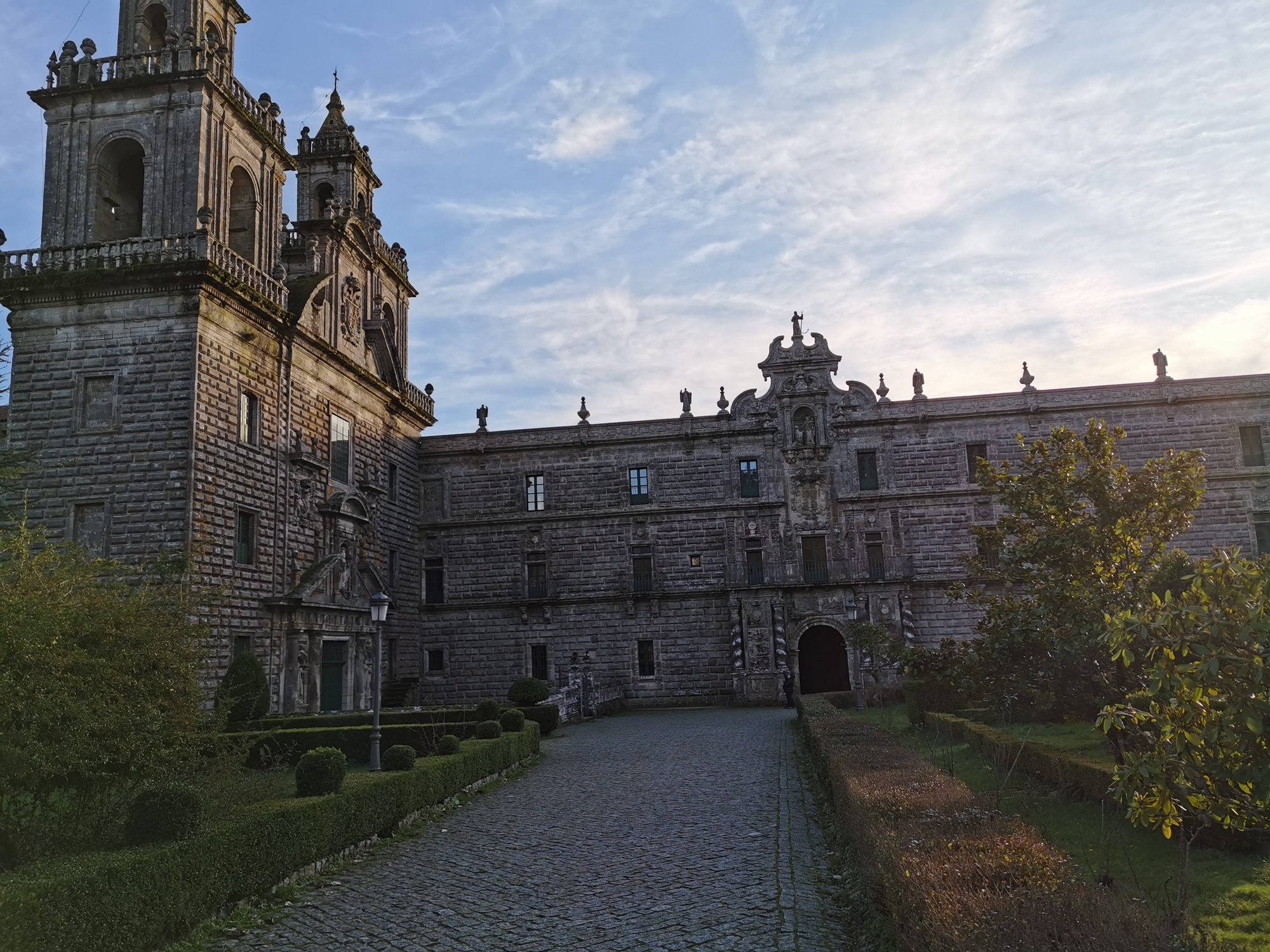 Fachada barroca de piedra y jardines del Monasterio de Oseira bajo el cielo.