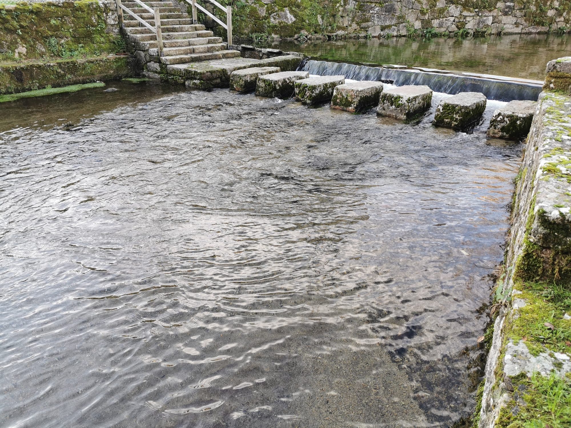 Pasaderas de piedra y escaleras sobre aguas cristalinas de un río en O Castro.