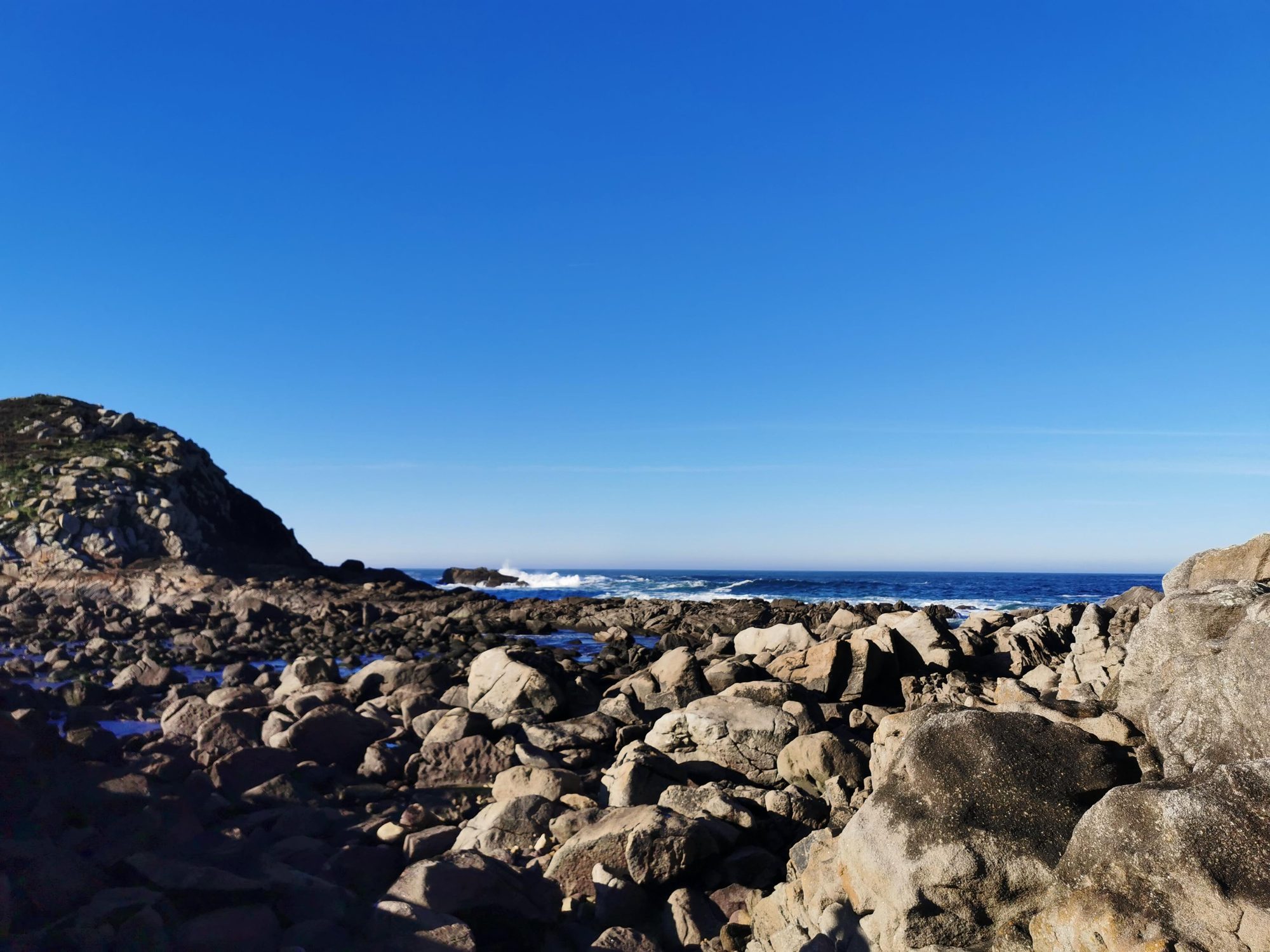 Costa rocosa de granito junto al mar azul bajo un cielo despejado.