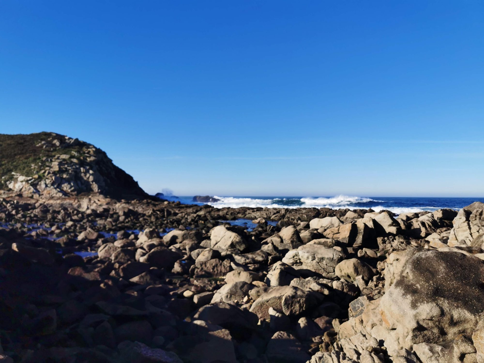 Costa rocosa junto al mar azul con olas rompiendo bajo cielo despejado.