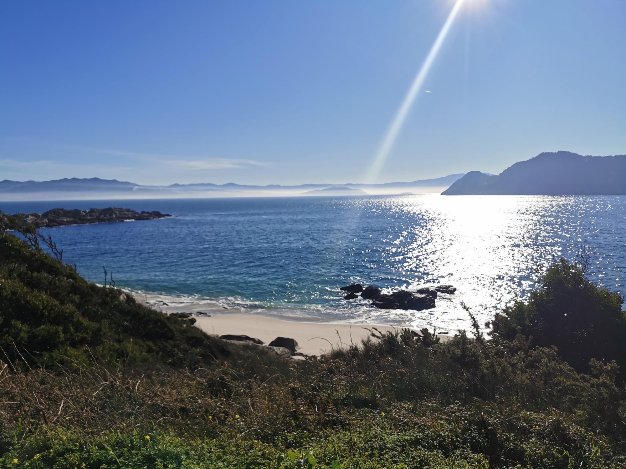 Pequeña cala de arena con el mar reluciente bajo el sol en la costa.