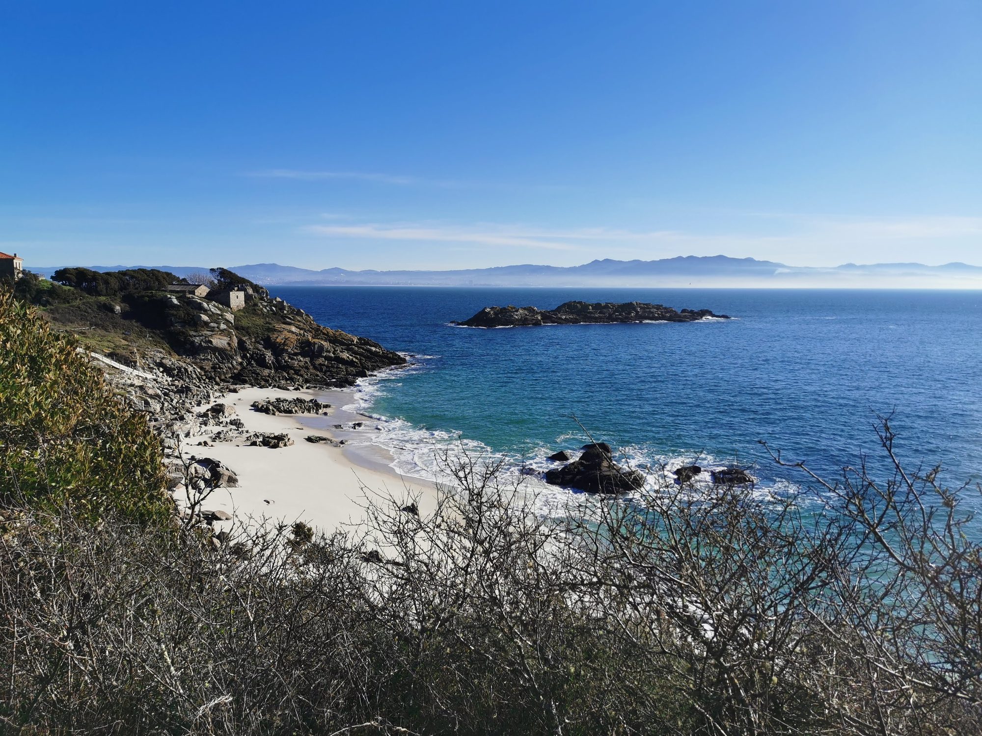 Cala de arena blanca rodeada de acantilados rocosos y mar azul en Vigo.