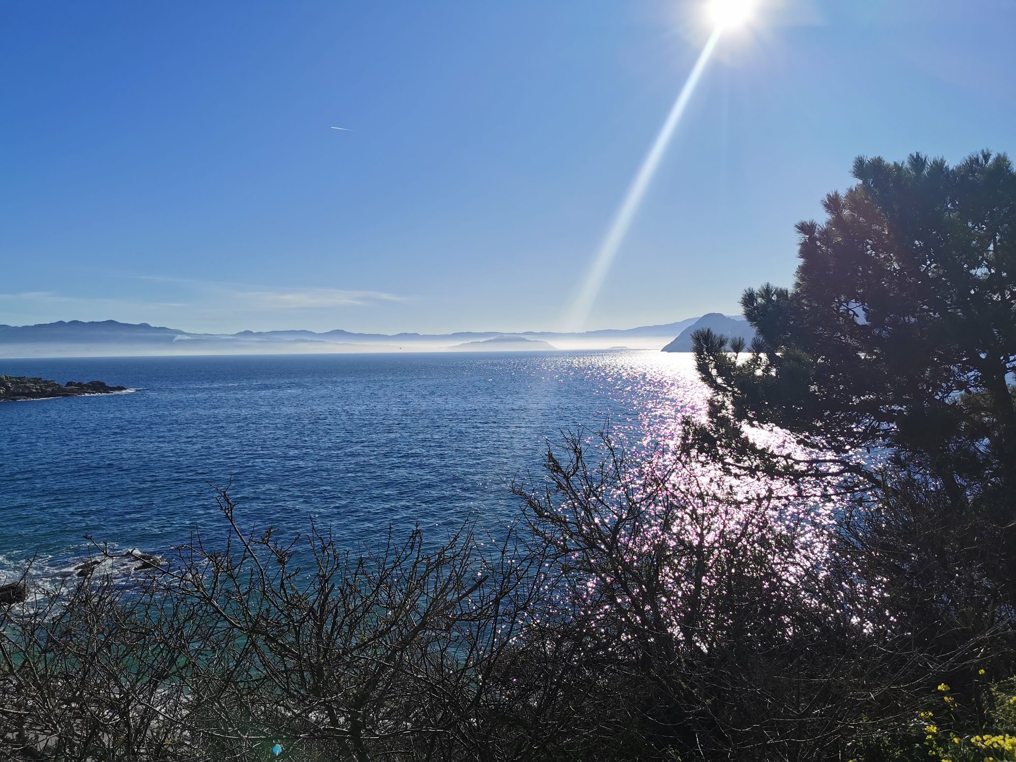 Vista de la ría de Vigo con destellos de sol en el mar y montañas lejanas.