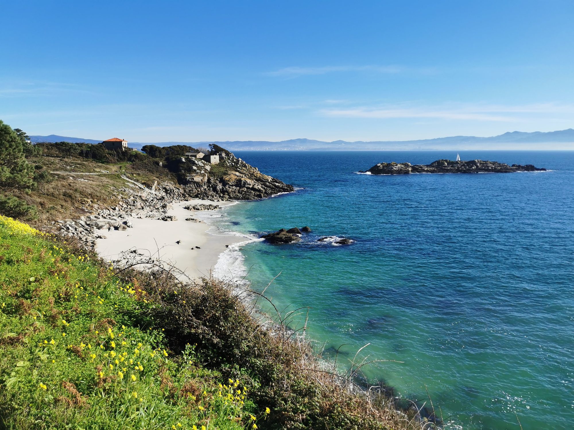 Cala de arena blanca y aguas turquesas entre acantilados rocosos frente al mar.