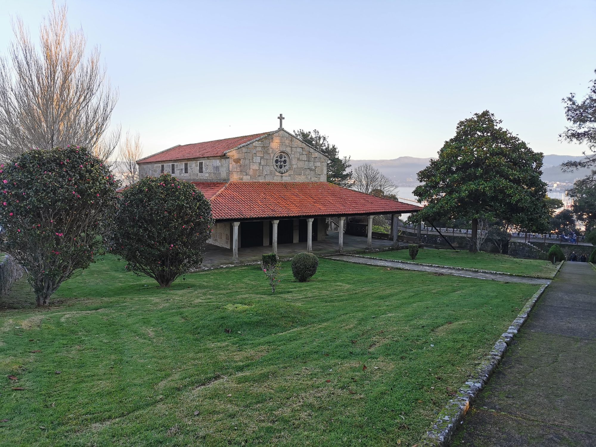 Ermita de piedra tradicional con tejado rojo rodeada de jardines en Baiona.
