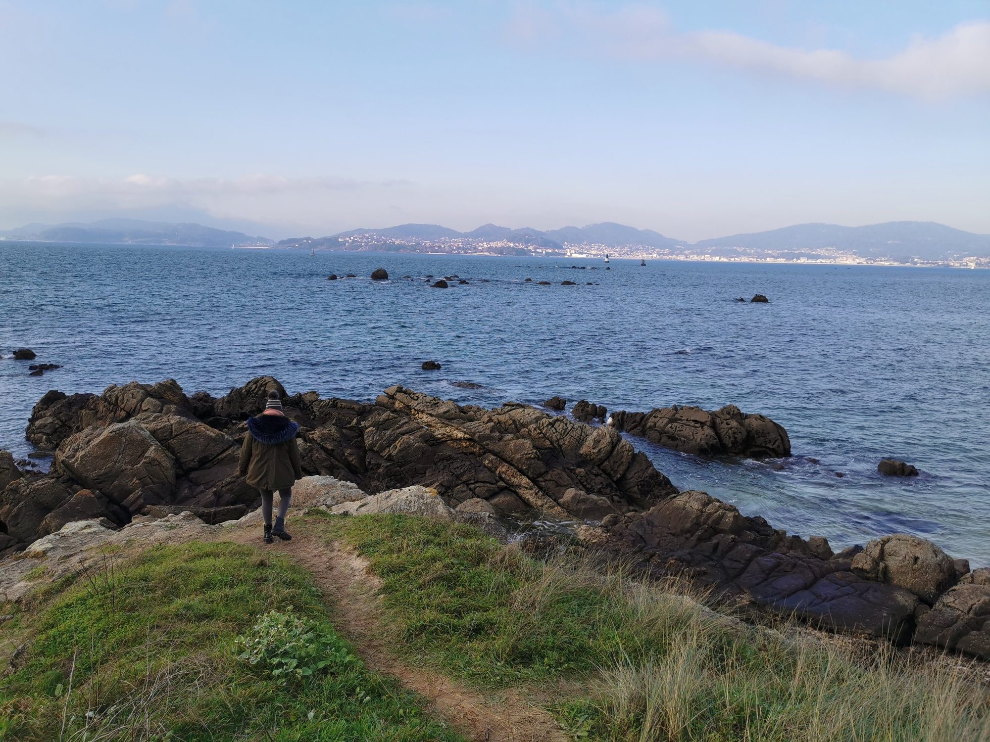 Persona caminando por un sendero rocoso frente al mar en la ría de Vigo.